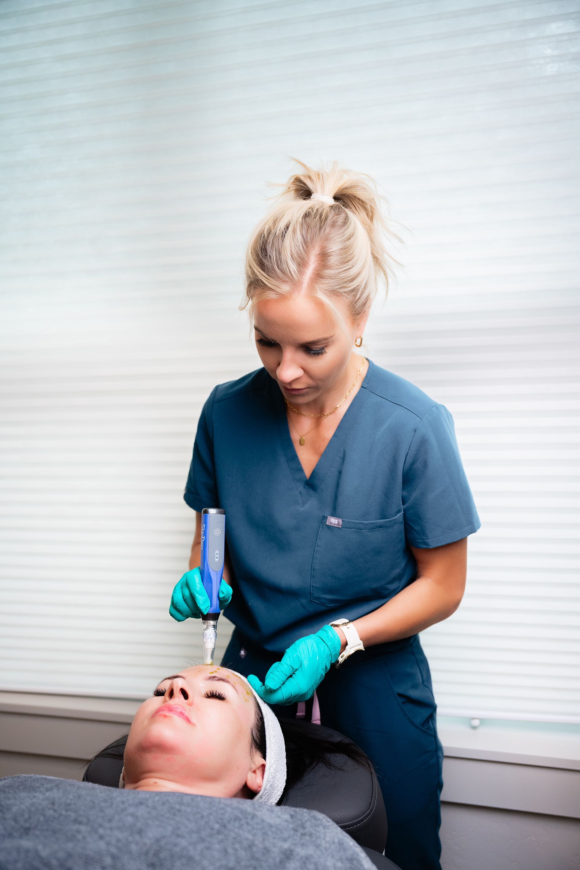 Esthetician with teal gloves applying treatment to a client’s face in a spa setting