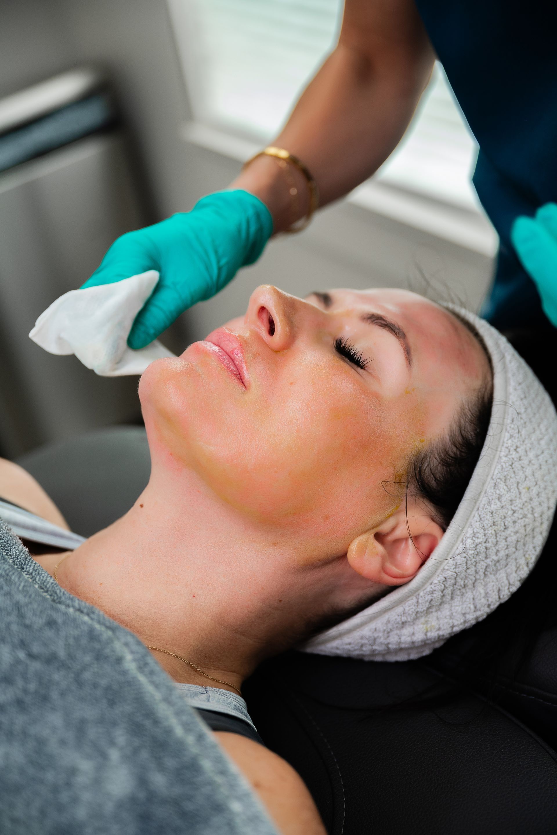Esthetician wipes a client’s face with a cloth during a facial treatment