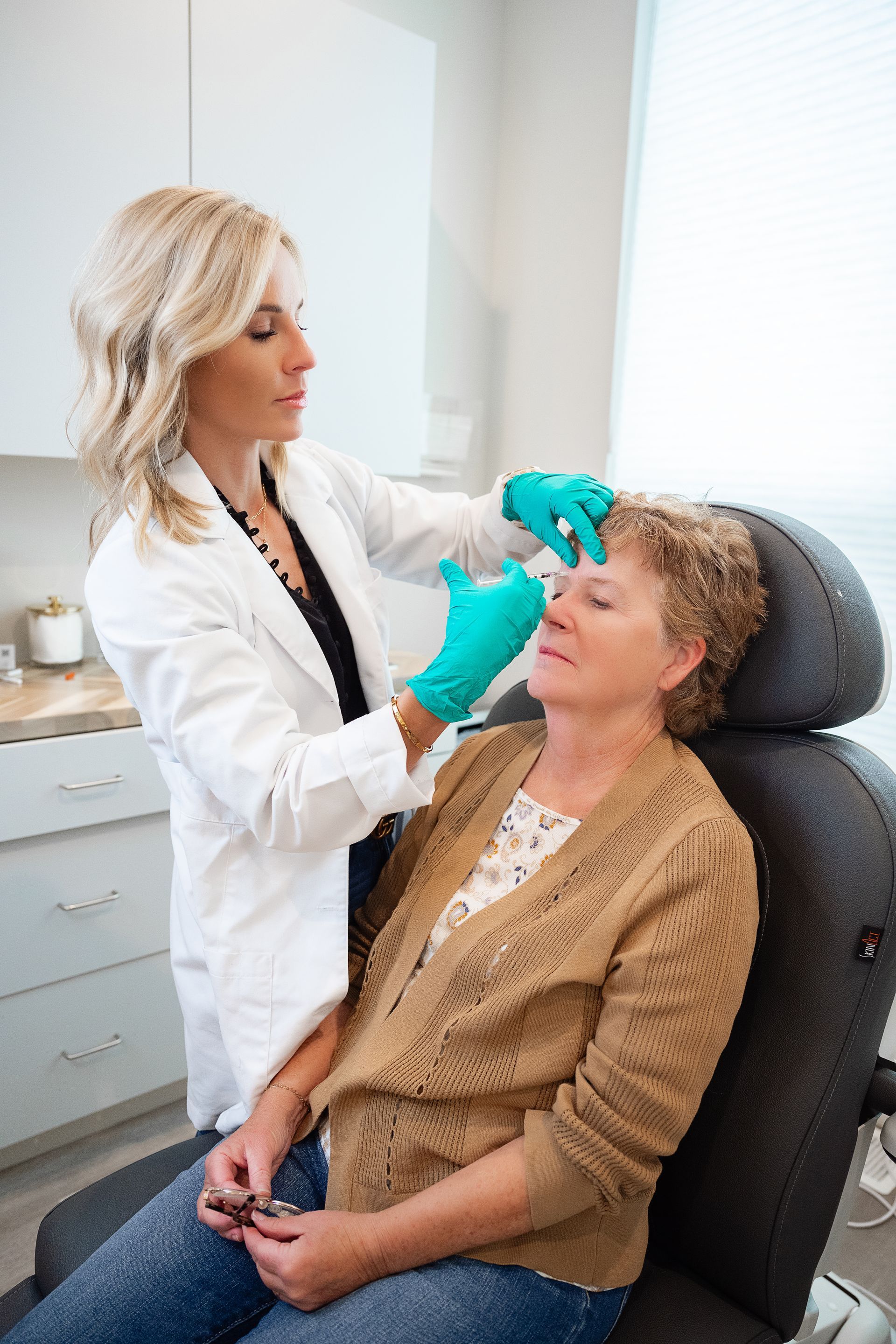 A woman is getting an injection in her forehead from a doctor.