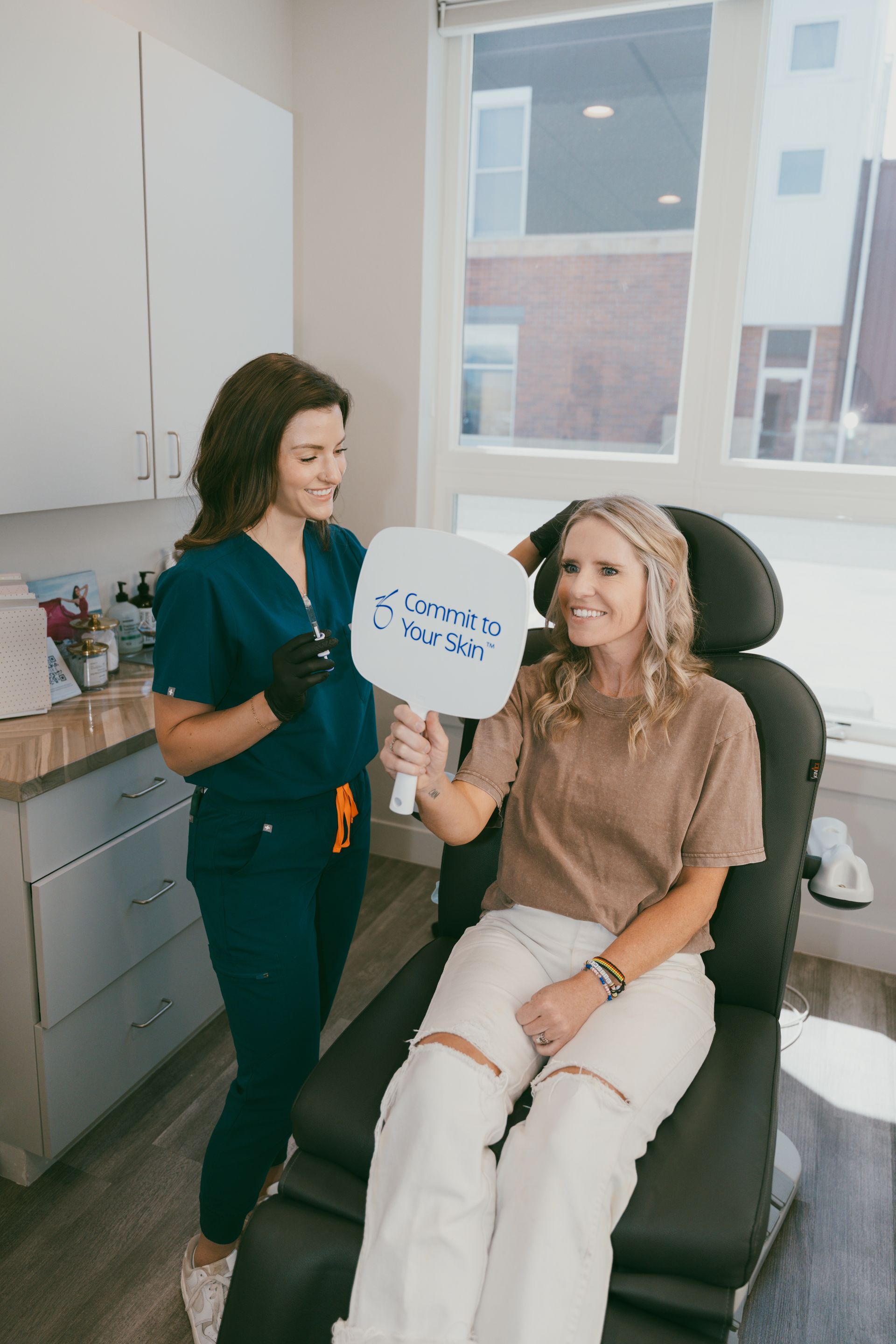 A female doctor examines a patient's neck in a medical office. The doctor wears a lab coat and the patient sits in a chair.