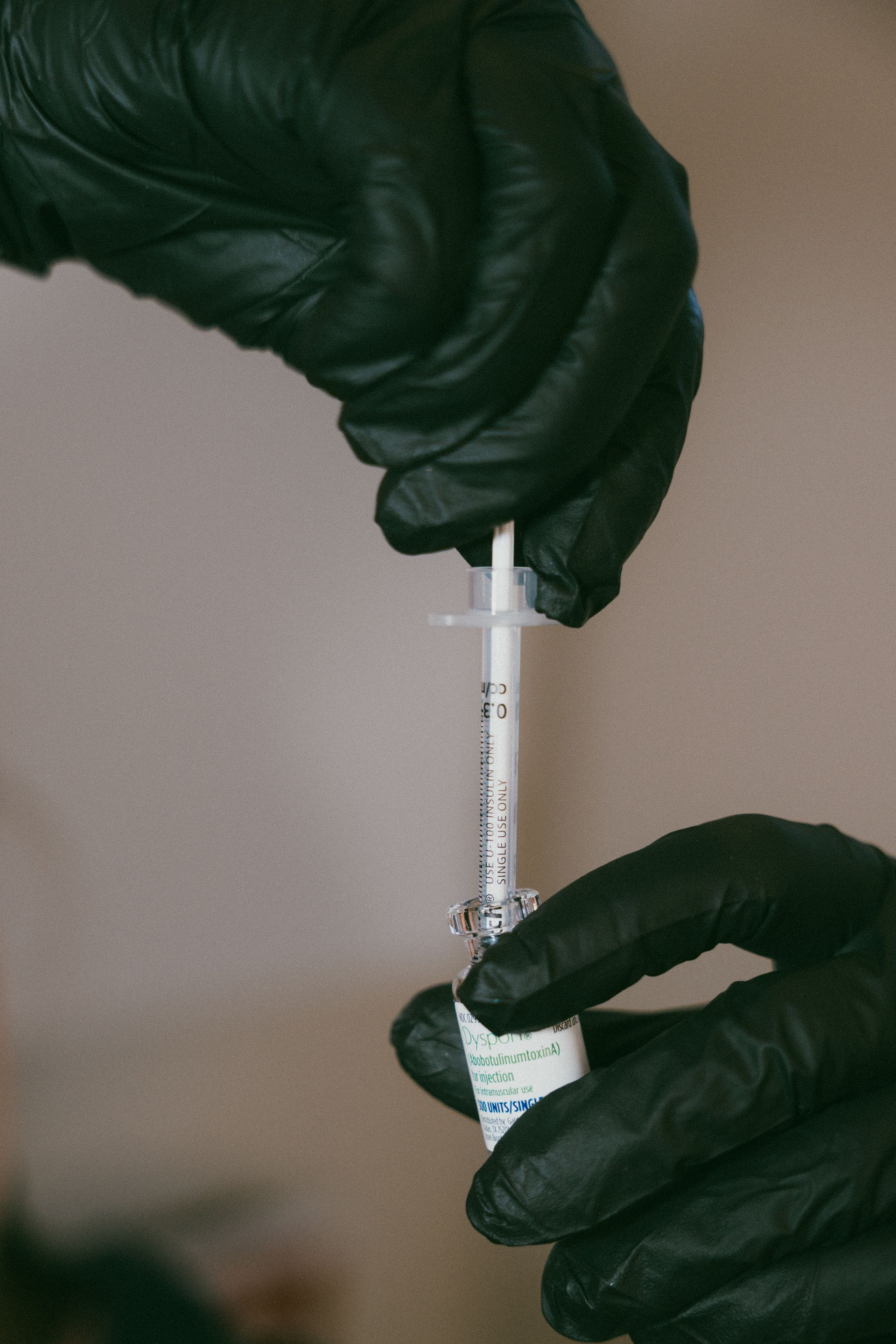 Hands in black gloves filling a syringe from a vial.