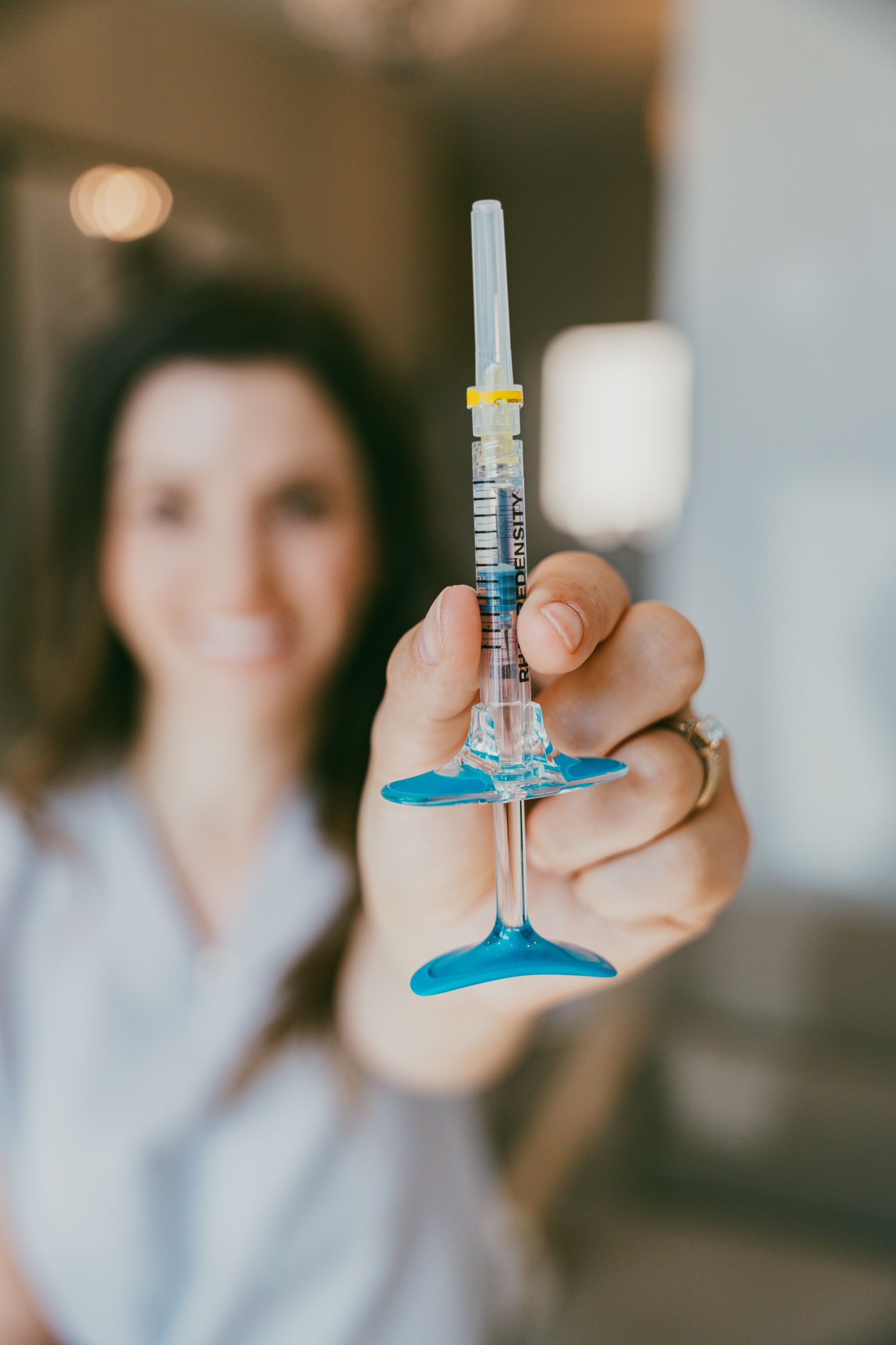 Woman holding a syringe filled with liquid; blue stabilizers. Blurred background.