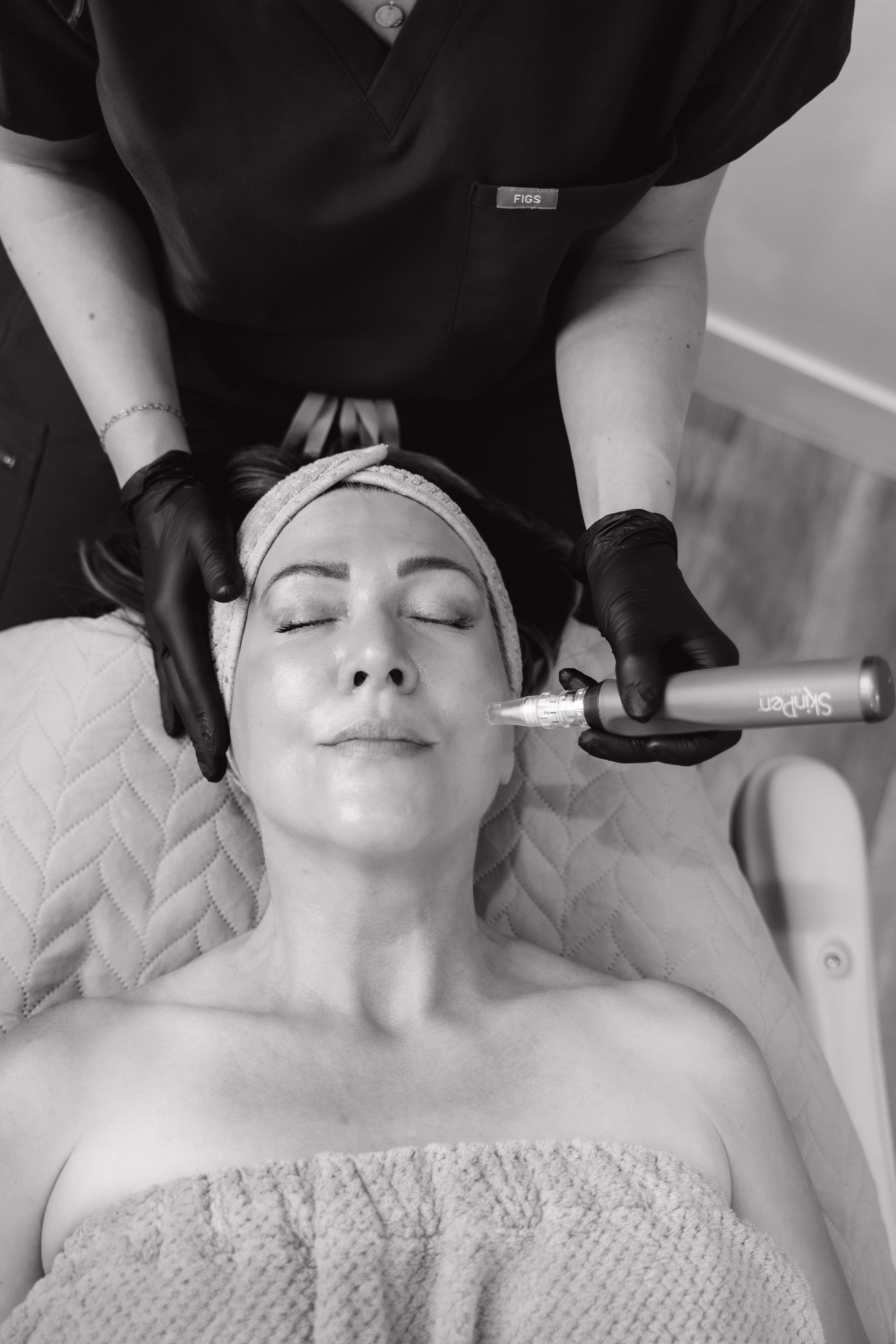 Woman receiving facial treatment with a handheld device, performed by a person wearing gloves in a spa setting.