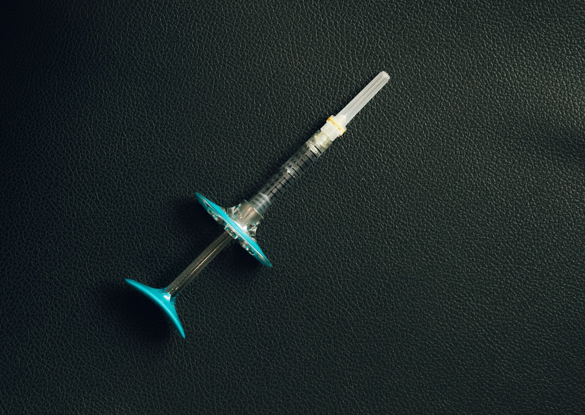 A syringe is sitting on a black surface.