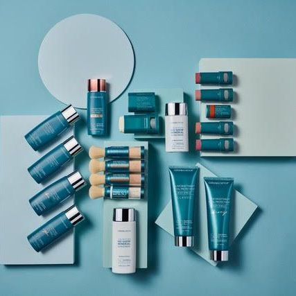 A bottle of serum , a bottle of cream , and a bottle of lotion are on a blue podium.