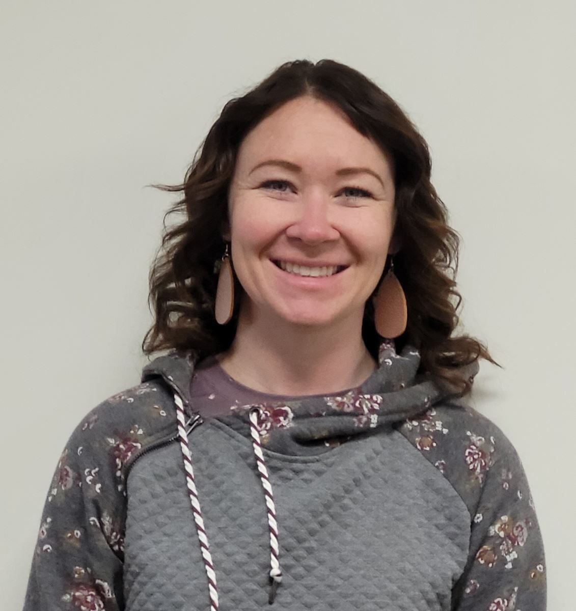 A woman wearing a grey hoodie and earrings smiles for the camera