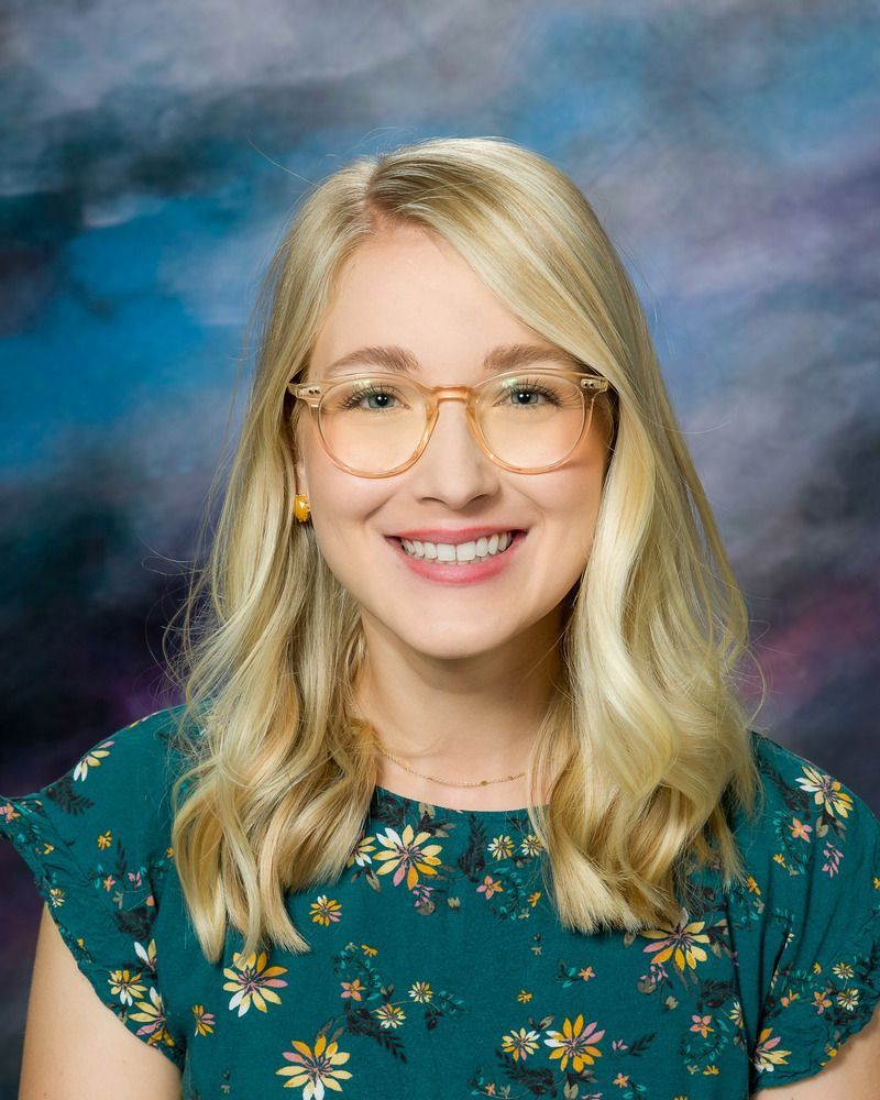 A woman wearing glasses and a floral shirt is smiling for the camera.