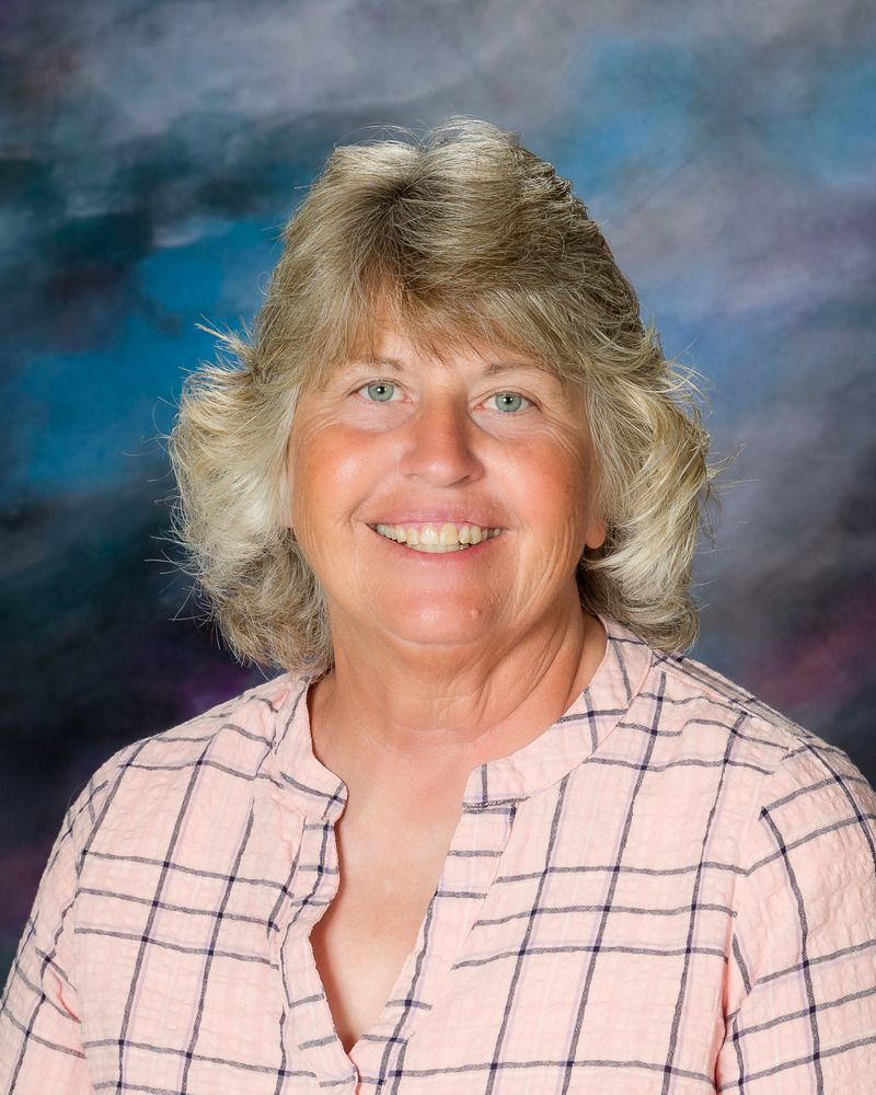 A woman in a pink plaid shirt is smiling for the camera.
