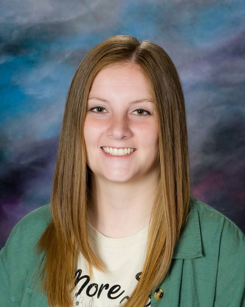 A young woman wearing a green jacket and a white shirt is smiling for the camera.