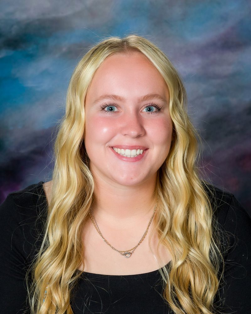 The woman is wearing a black shirt and a necklace and smiling for the camera.