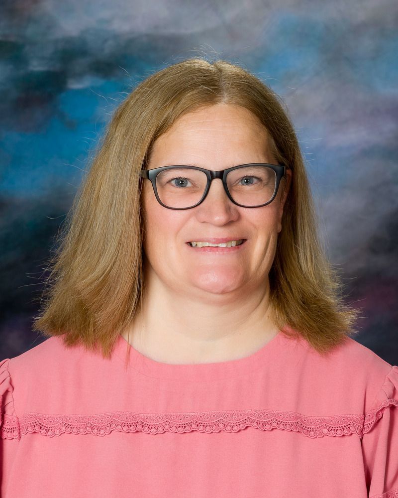 A woman wearing glasses and a pink shirt is smiling for the camera.