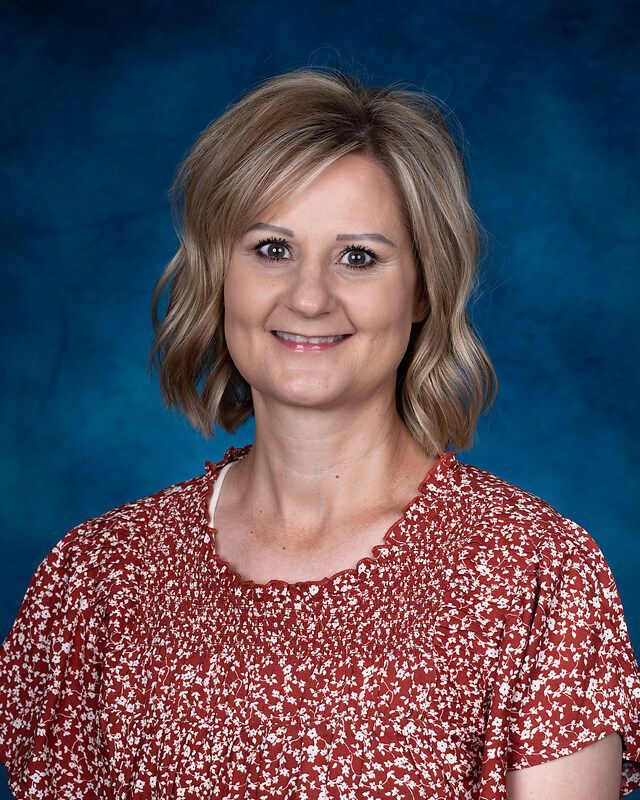 A woman in a red shirt is posing for a picture in front of a blue background.