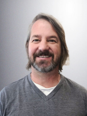 A man with long hair and a beard is smiling for the camera.