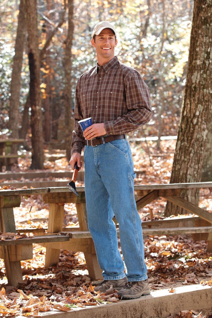 A man in a plaid shirt and blue jeans is standing in front of a picnic table.