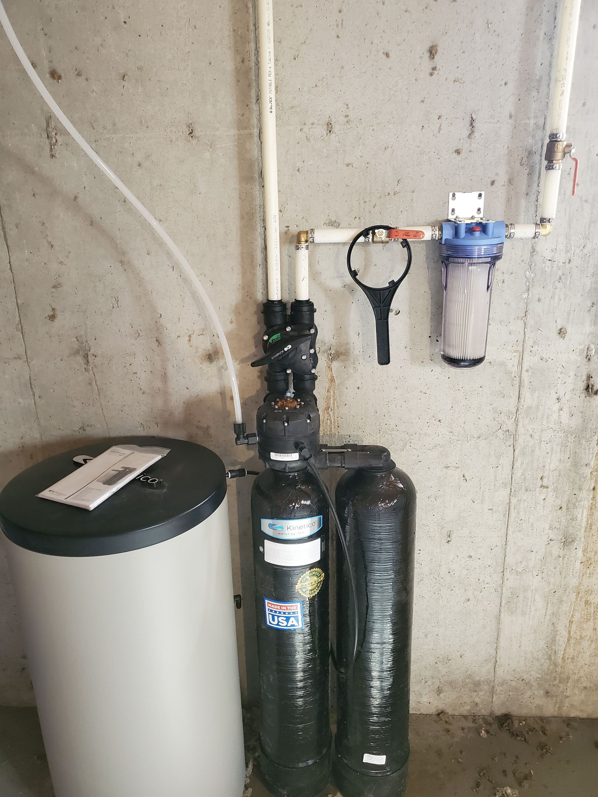 Water softener and filter system installed on a concrete wall. Includes tanks, filter housing, and connecting pipes.