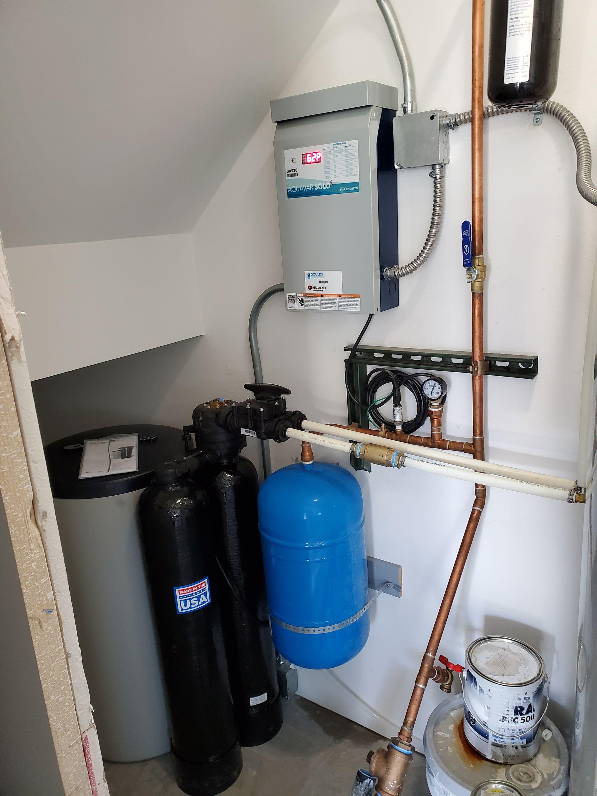 Water treatment and heating system in a utility closet with tanks, piping, and electrical components.