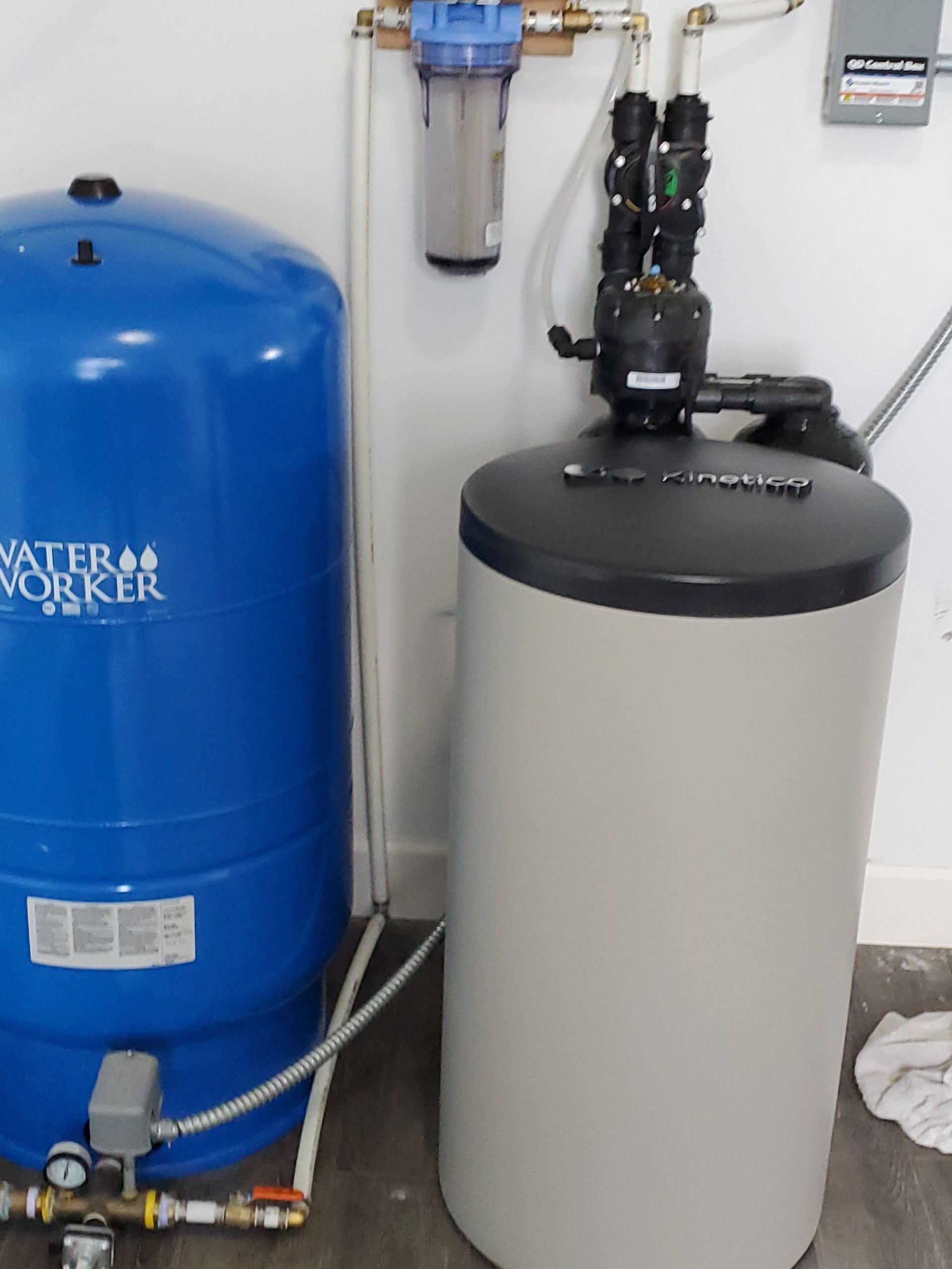 Water filtration system in a basement. Blue water tank, beige softener, and filter pipes.
