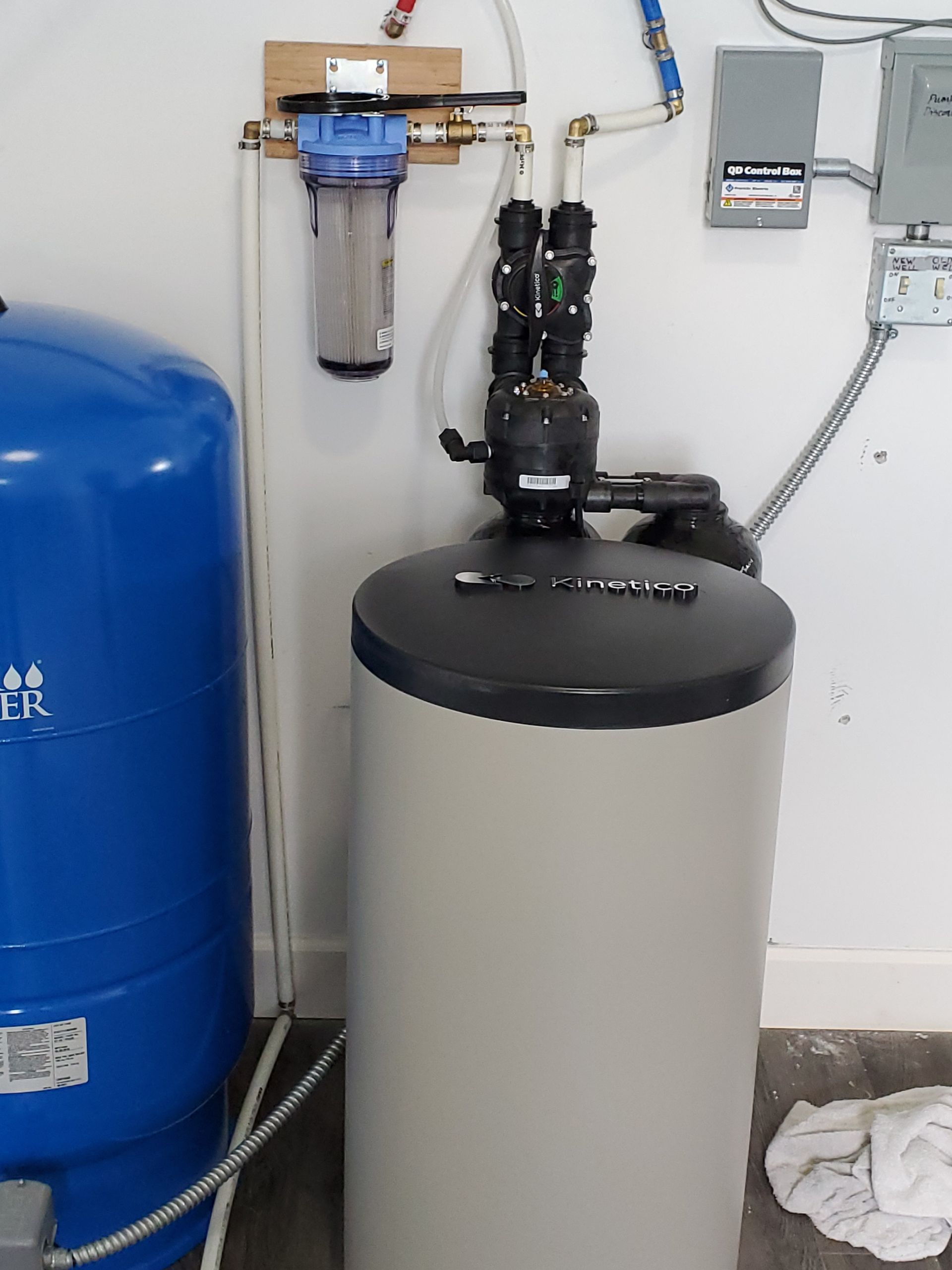 Water filtration and softener system installed indoors with blue pressure tank.