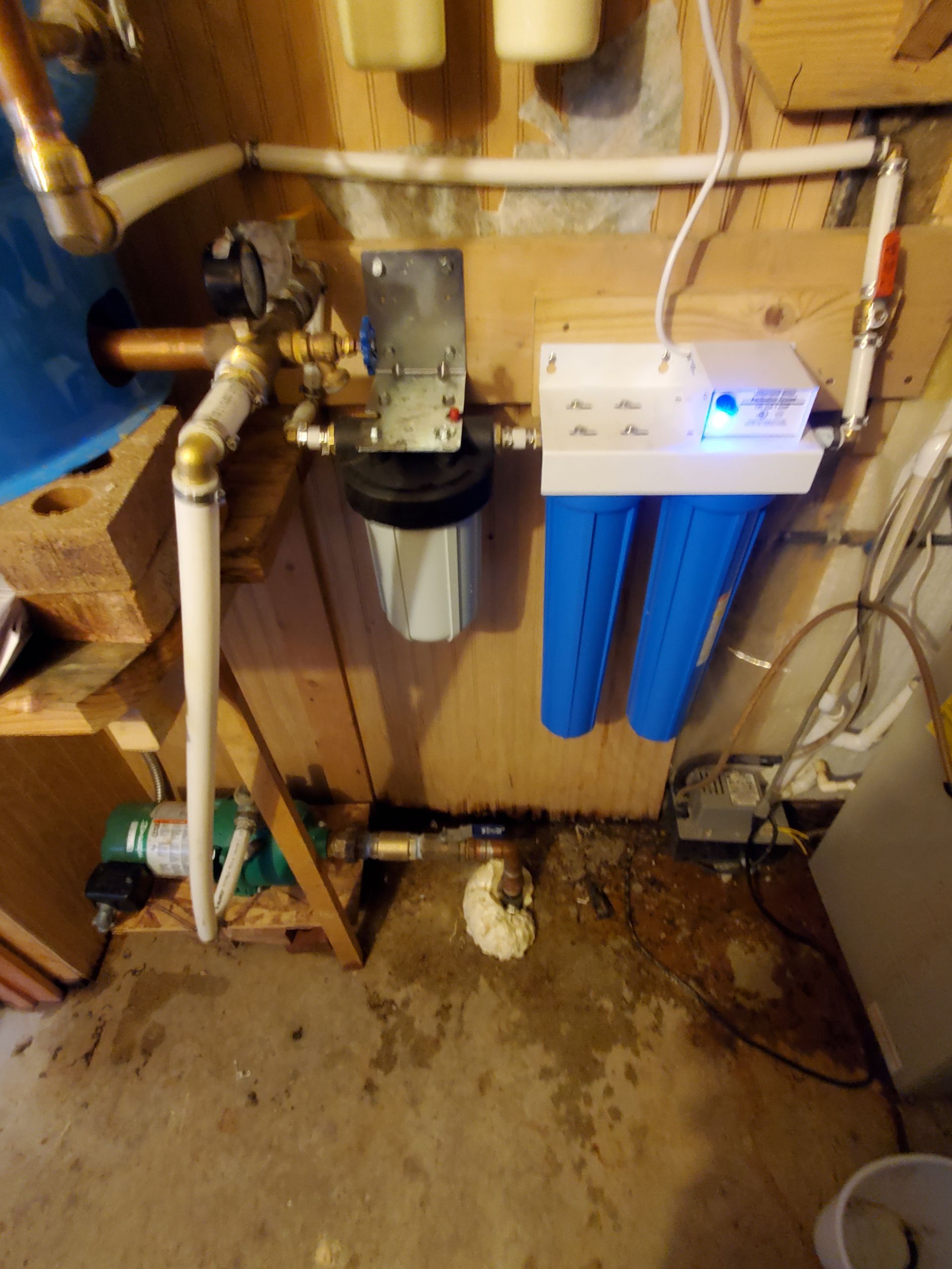 Water filtration system on a wooden wall, with blue and black filters, and connecting pipes.