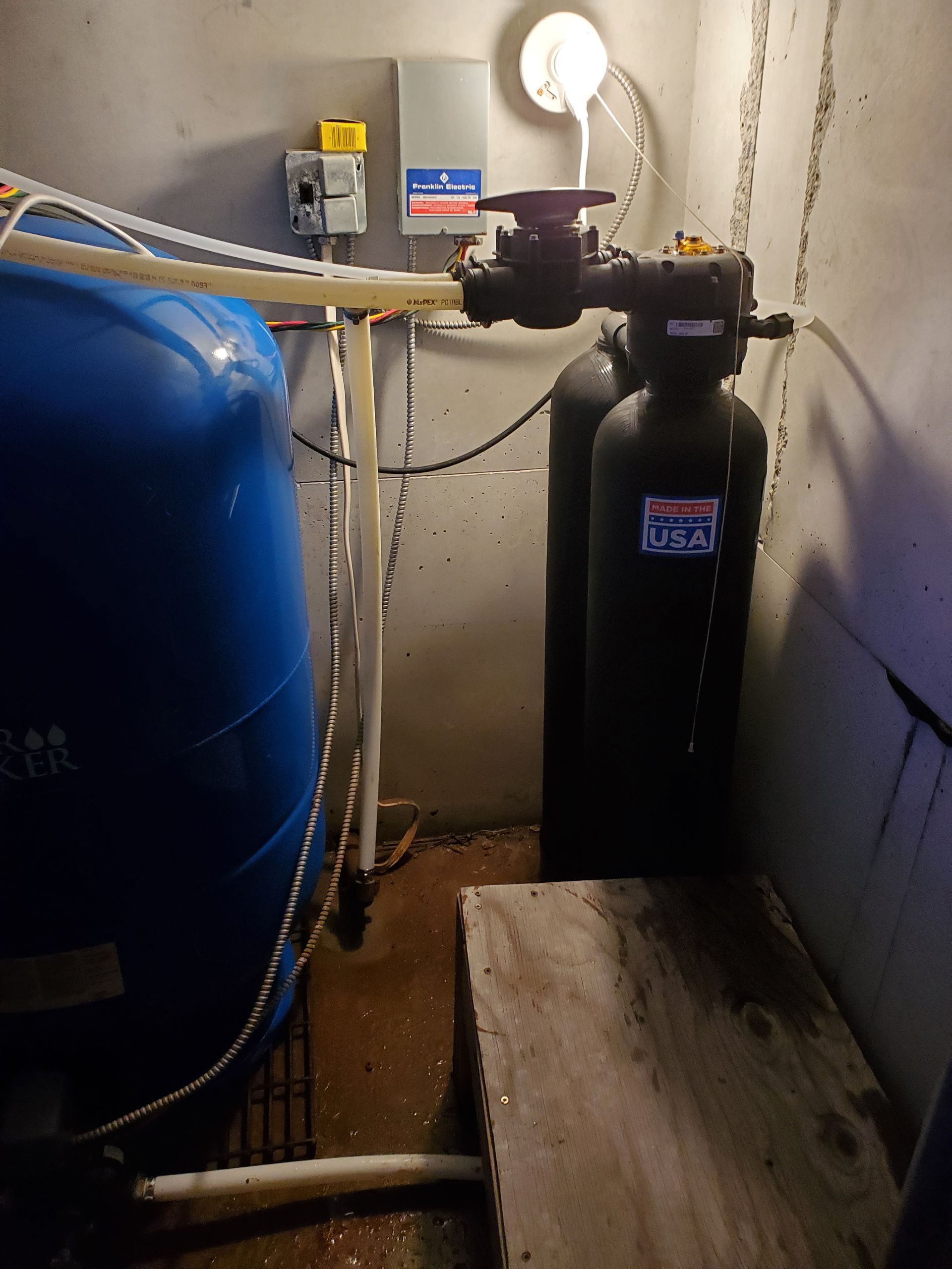 Water filtration system with blue tank, black tanks, and associated pipes and wiring in a basement.