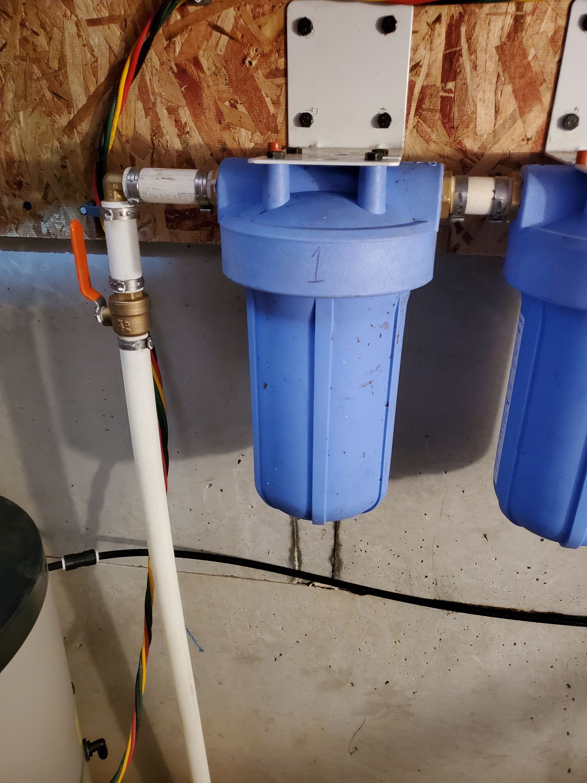 Blue water filter system installed on a concrete wall with white pipes and a brass valve.