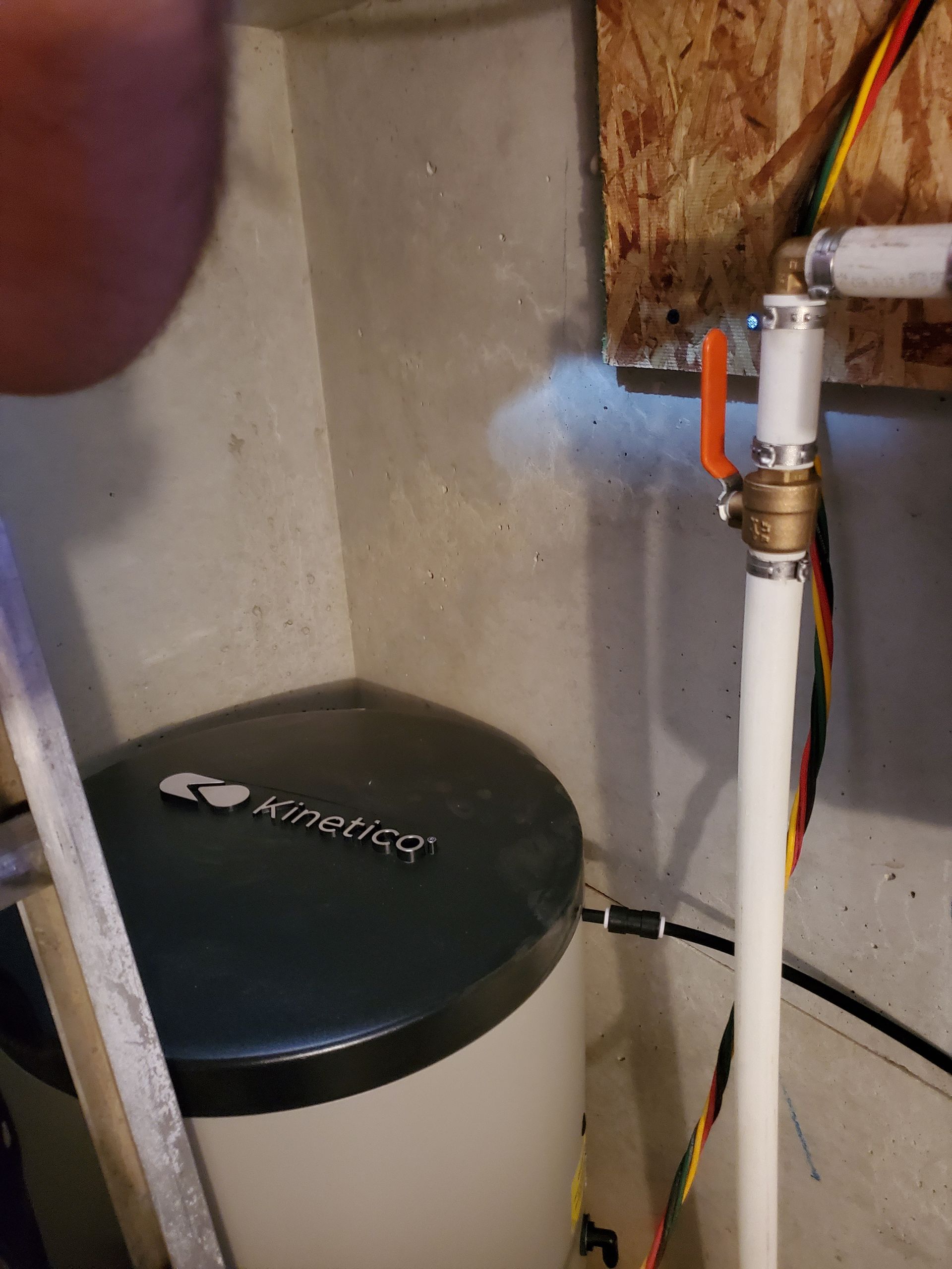 Water softener tank next to a concrete wall, with white pipes and a valve.