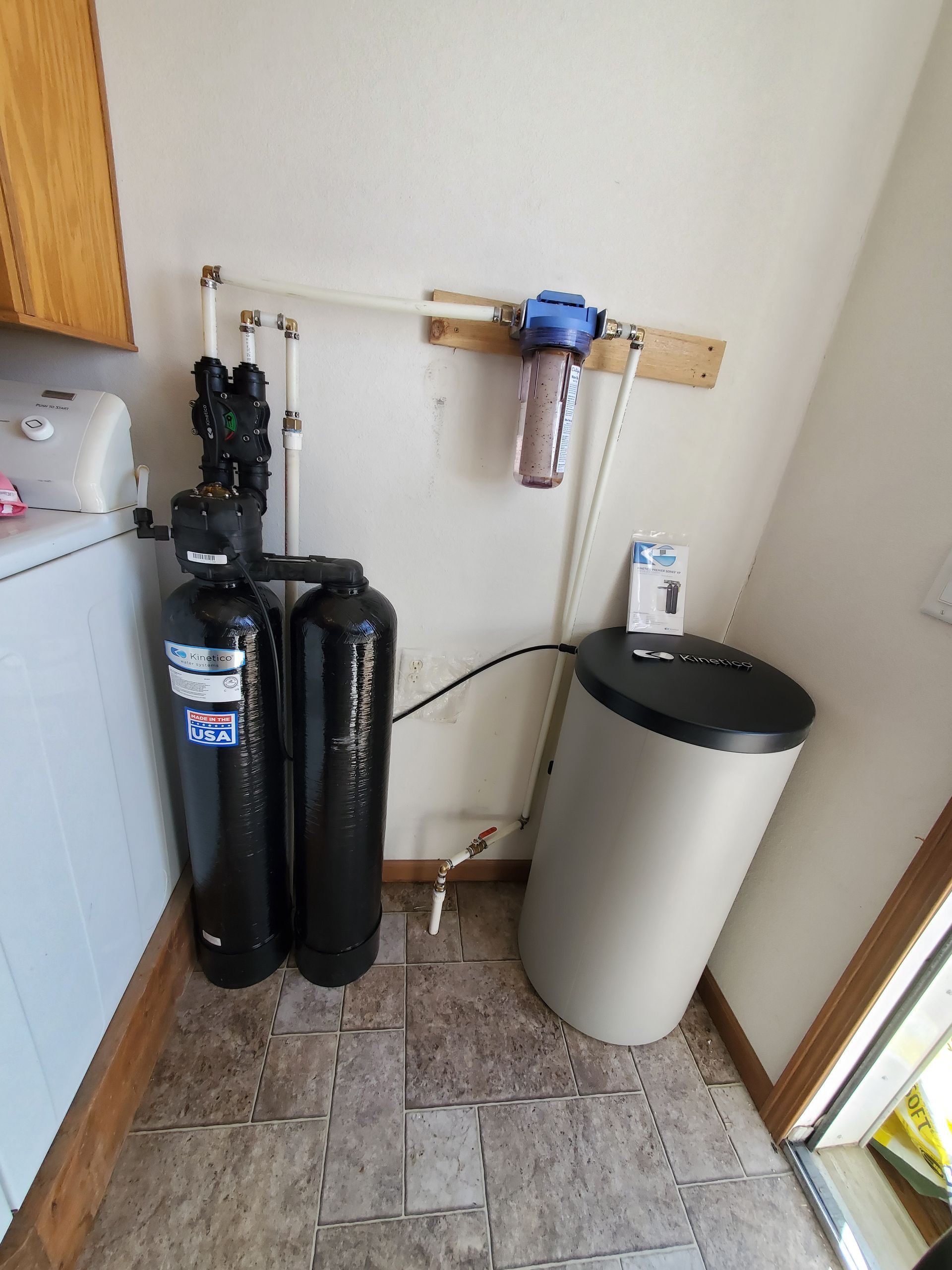 Water filtration system with black tanks, blue filter, and beige salt tank, in a utility room.