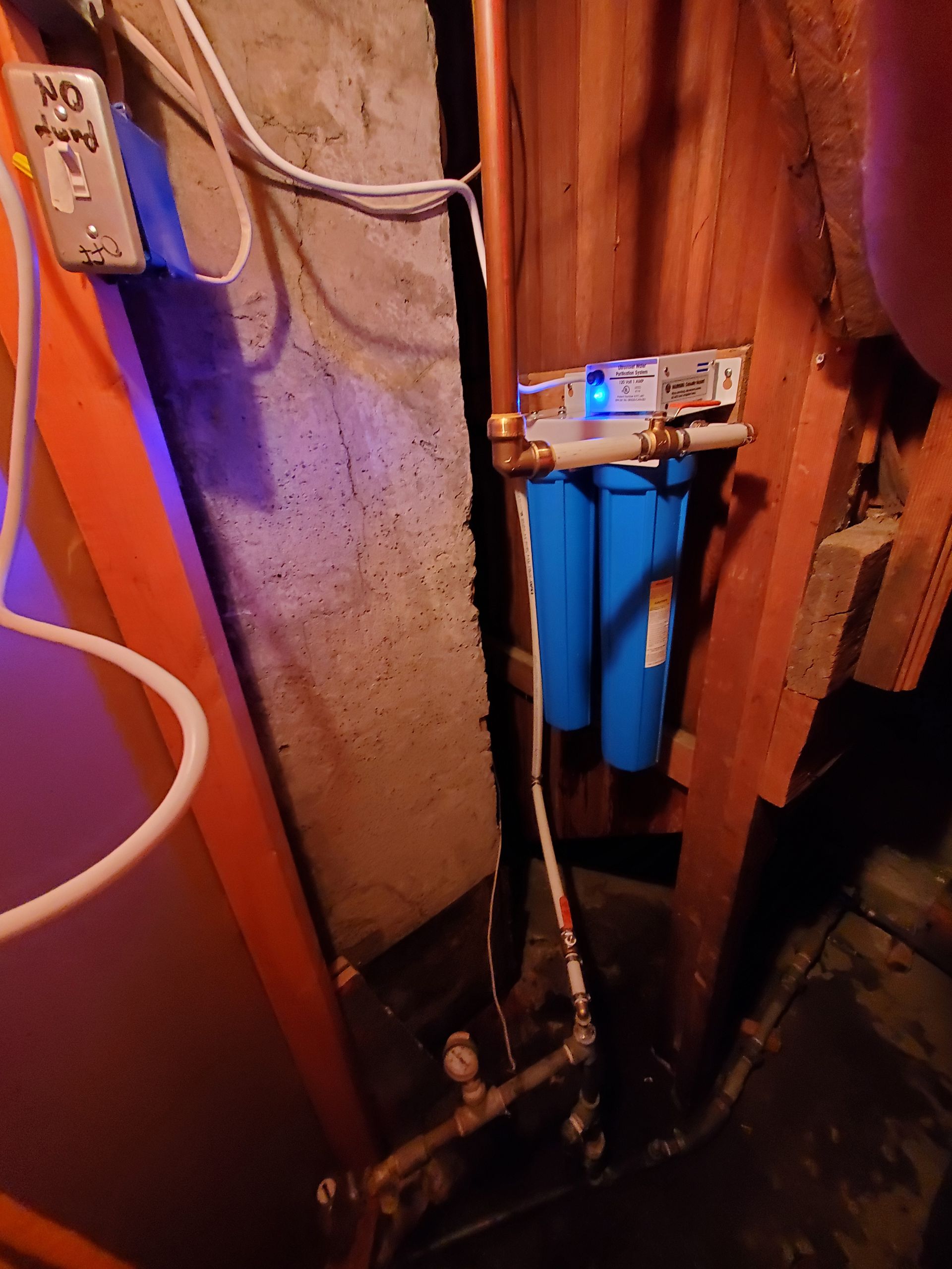 Water filtration system with blue filters, copper pipes, and electrical wiring in a basement.