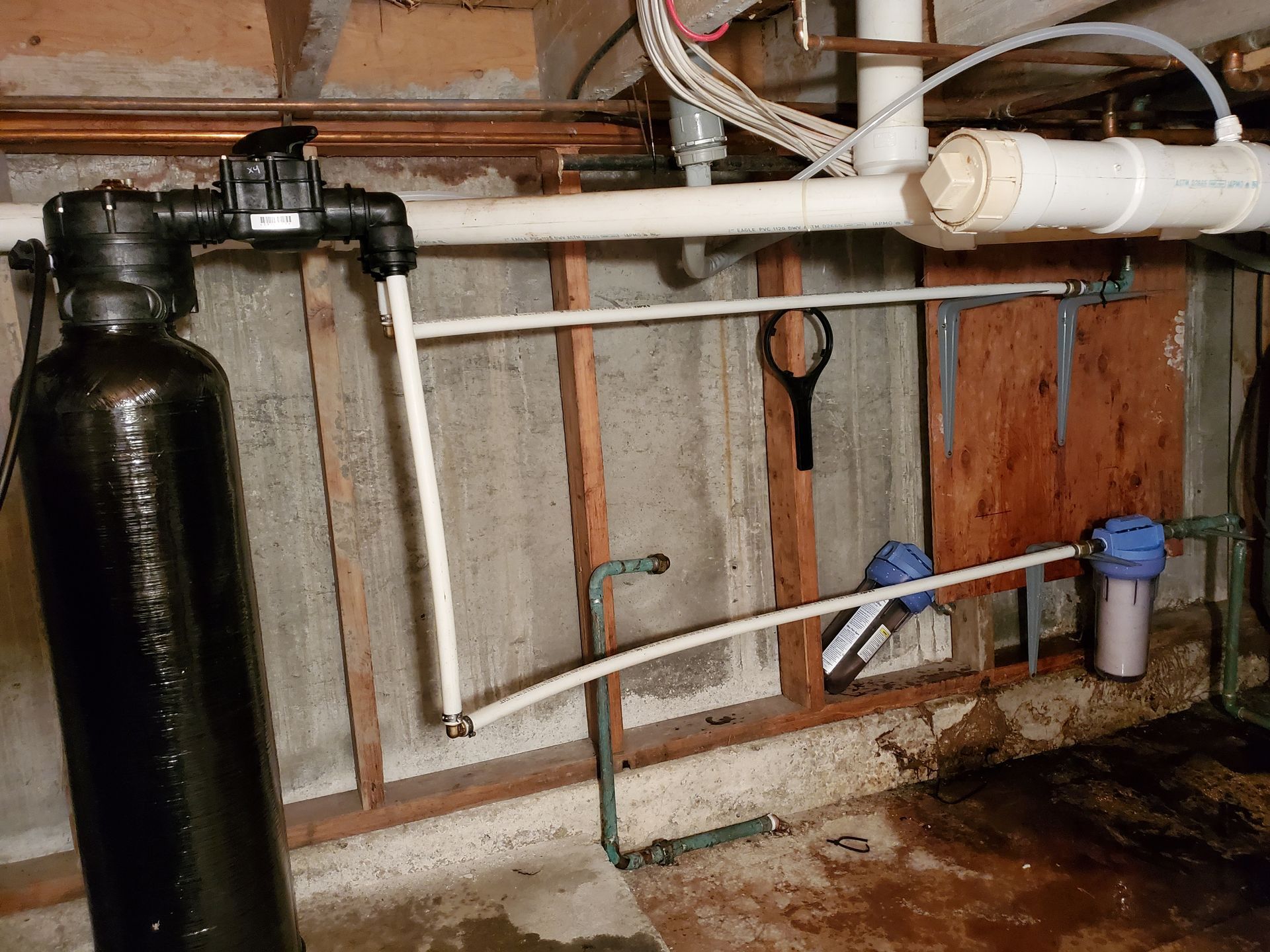 Water filtration system with black tank, white pipes, and blue filters in a basement.