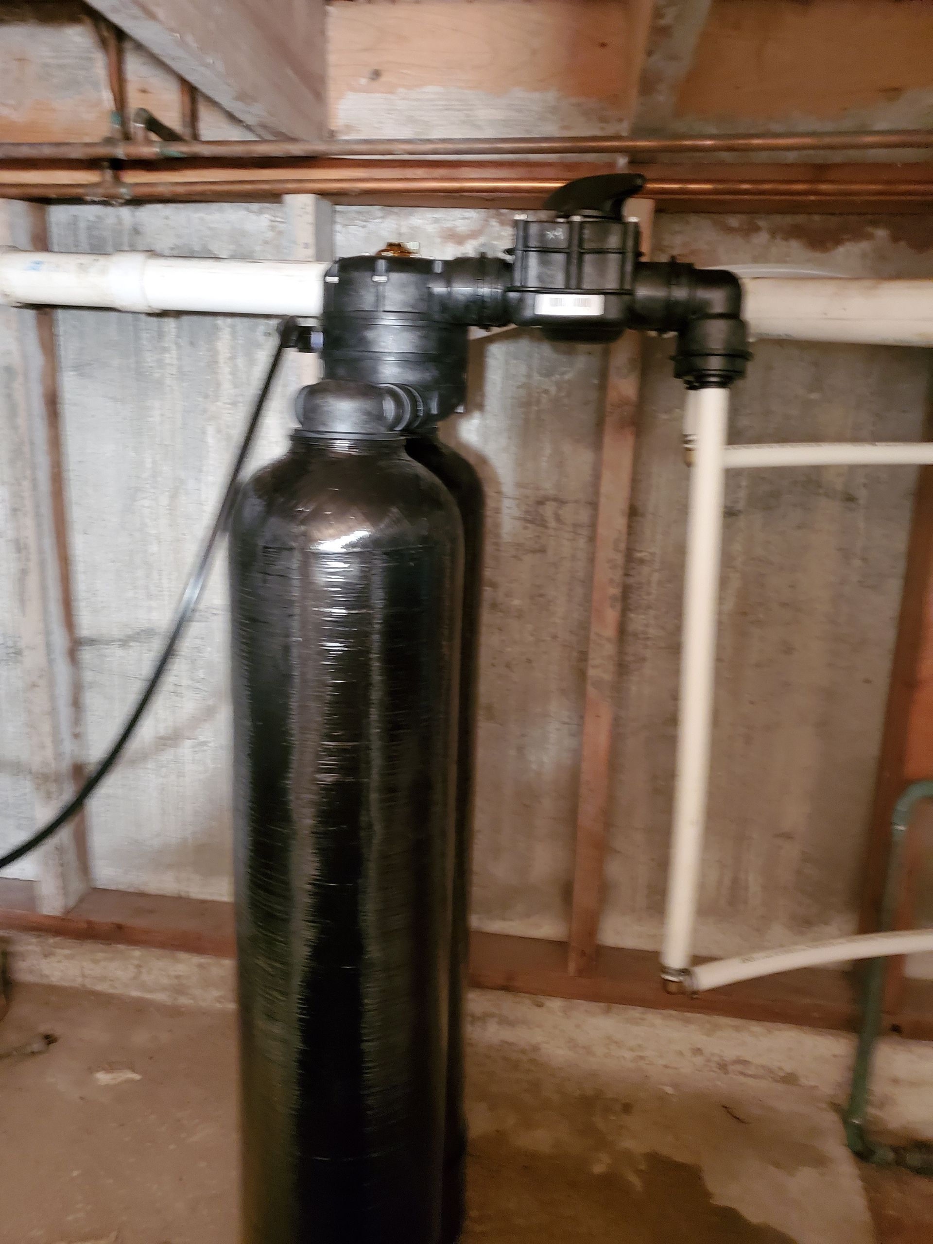 Black water filtration system installed against a concrete basement wall with connected pipes.