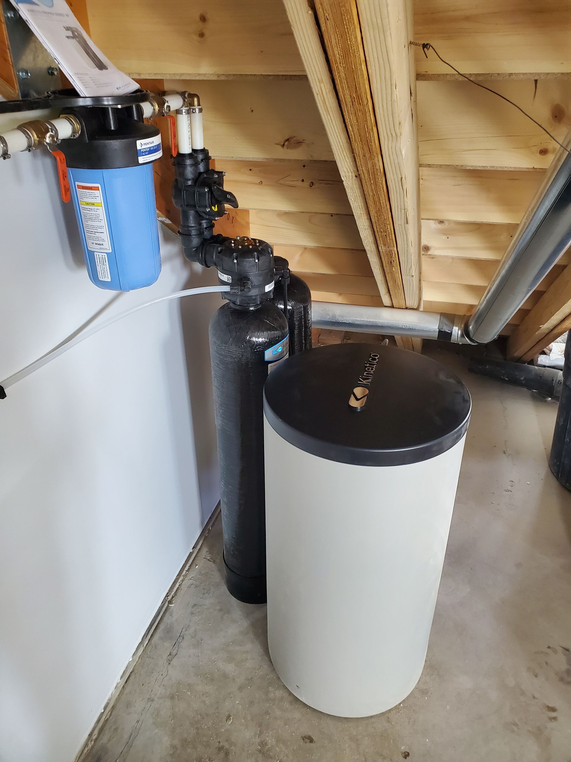 Water filtration system in a wooden attic space; includes filters, tank, and plumbing.
