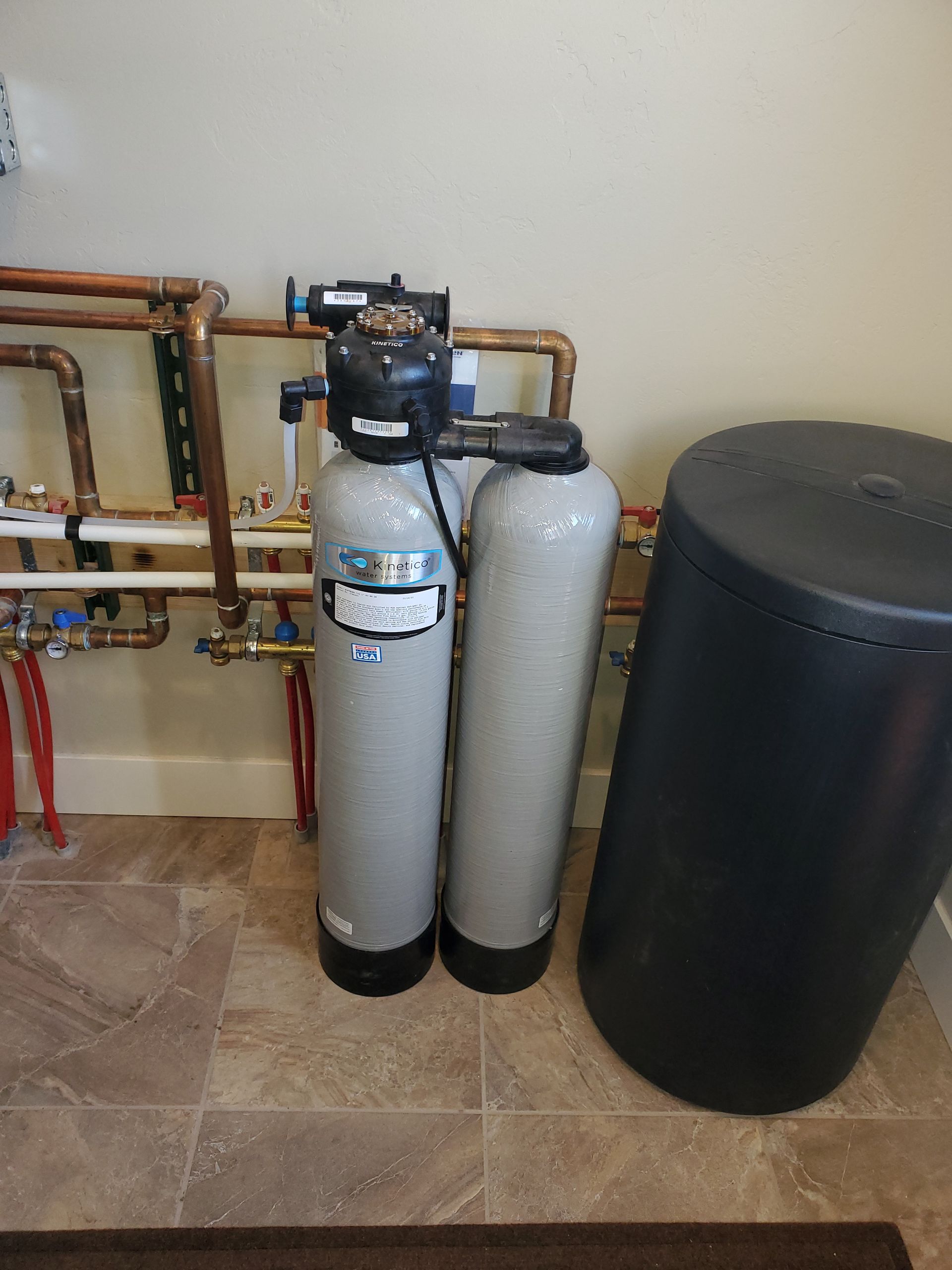 Two gray water filtration tanks and a black tank in a utility room with copper pipes.