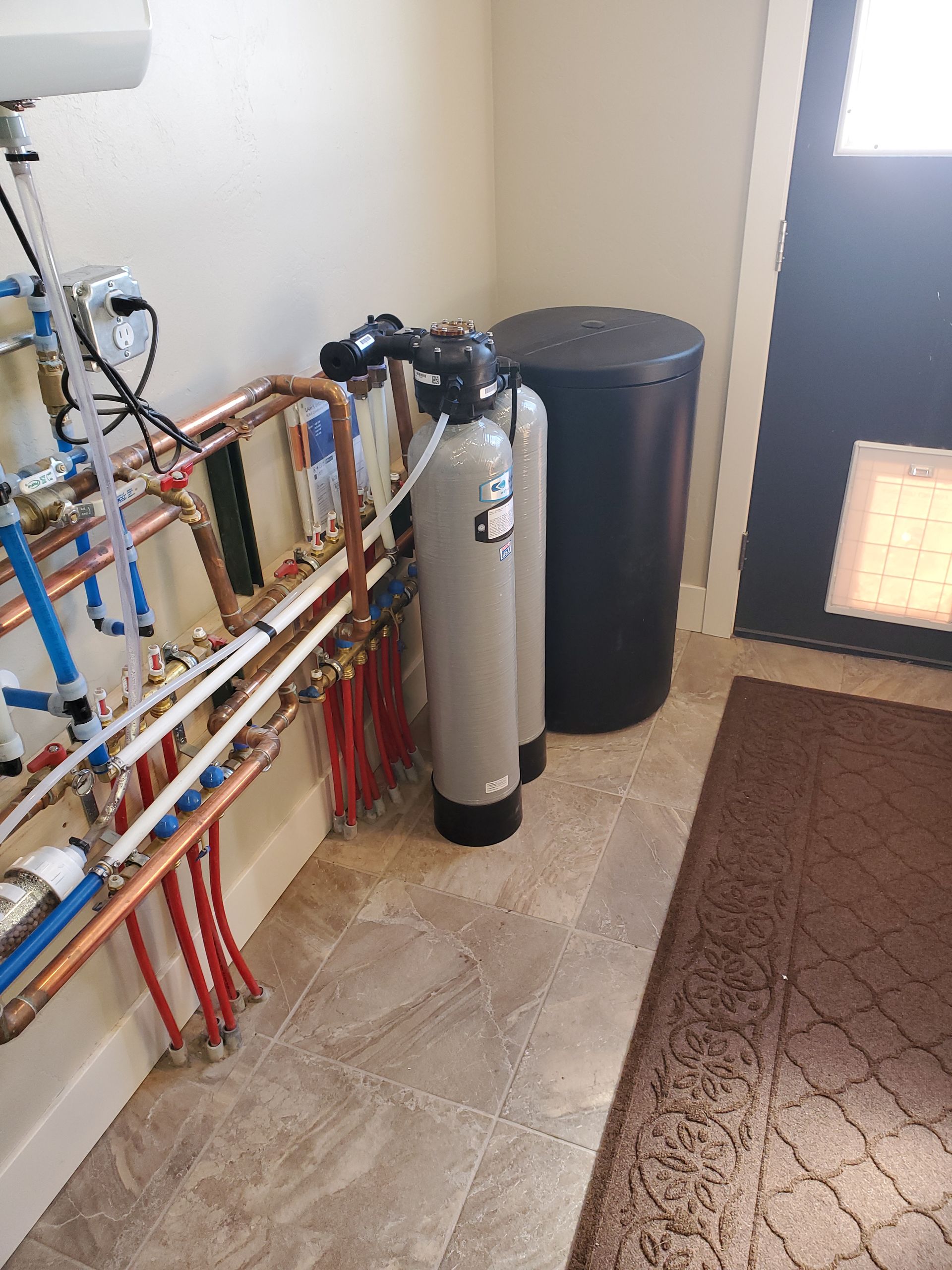 Water filtration system with copper pipes, tanks, and a black cylinder against a wall.