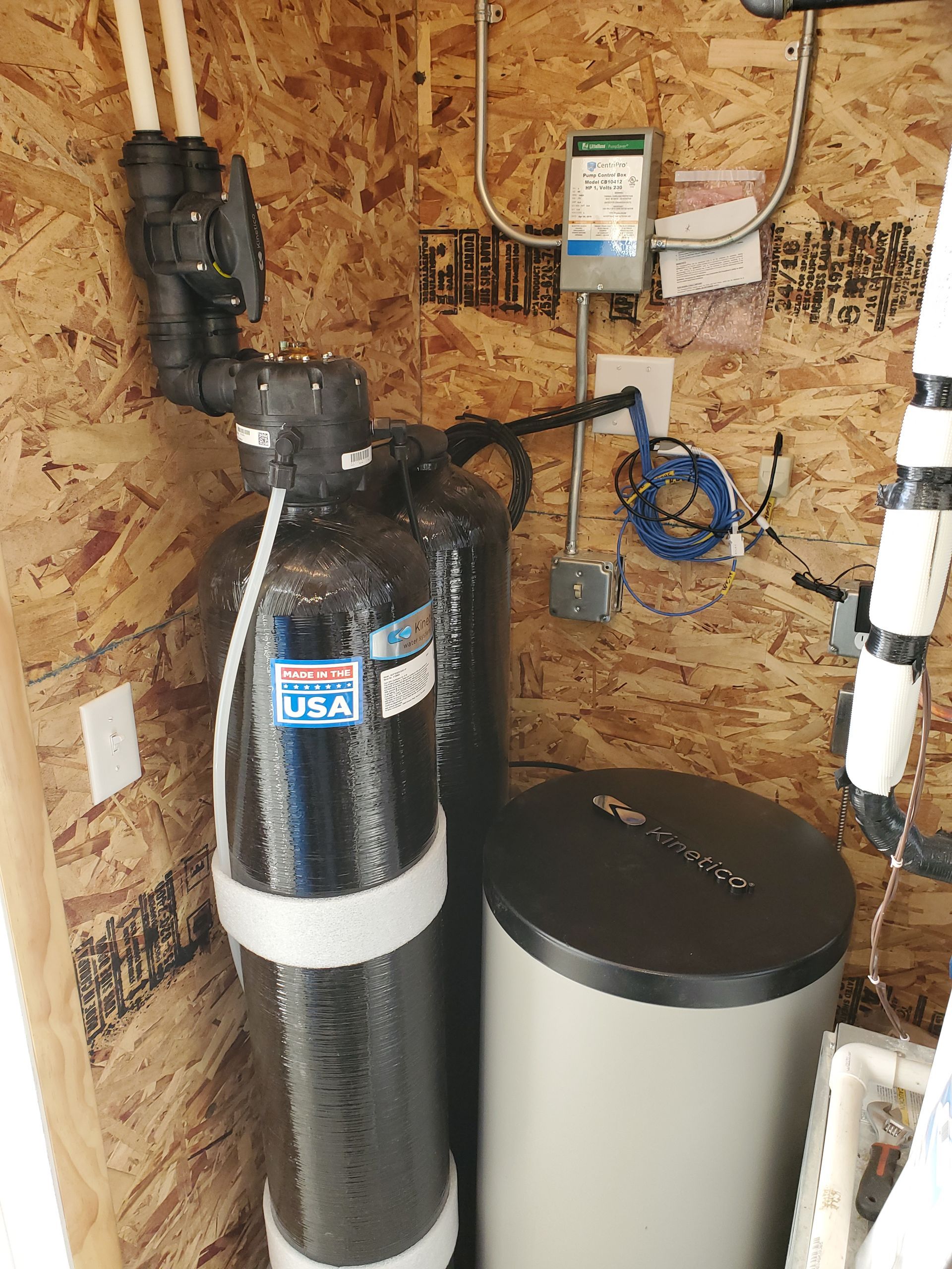 Water filtration system inside a small utility space. Includes black tanks, a gray tank, and white piping.