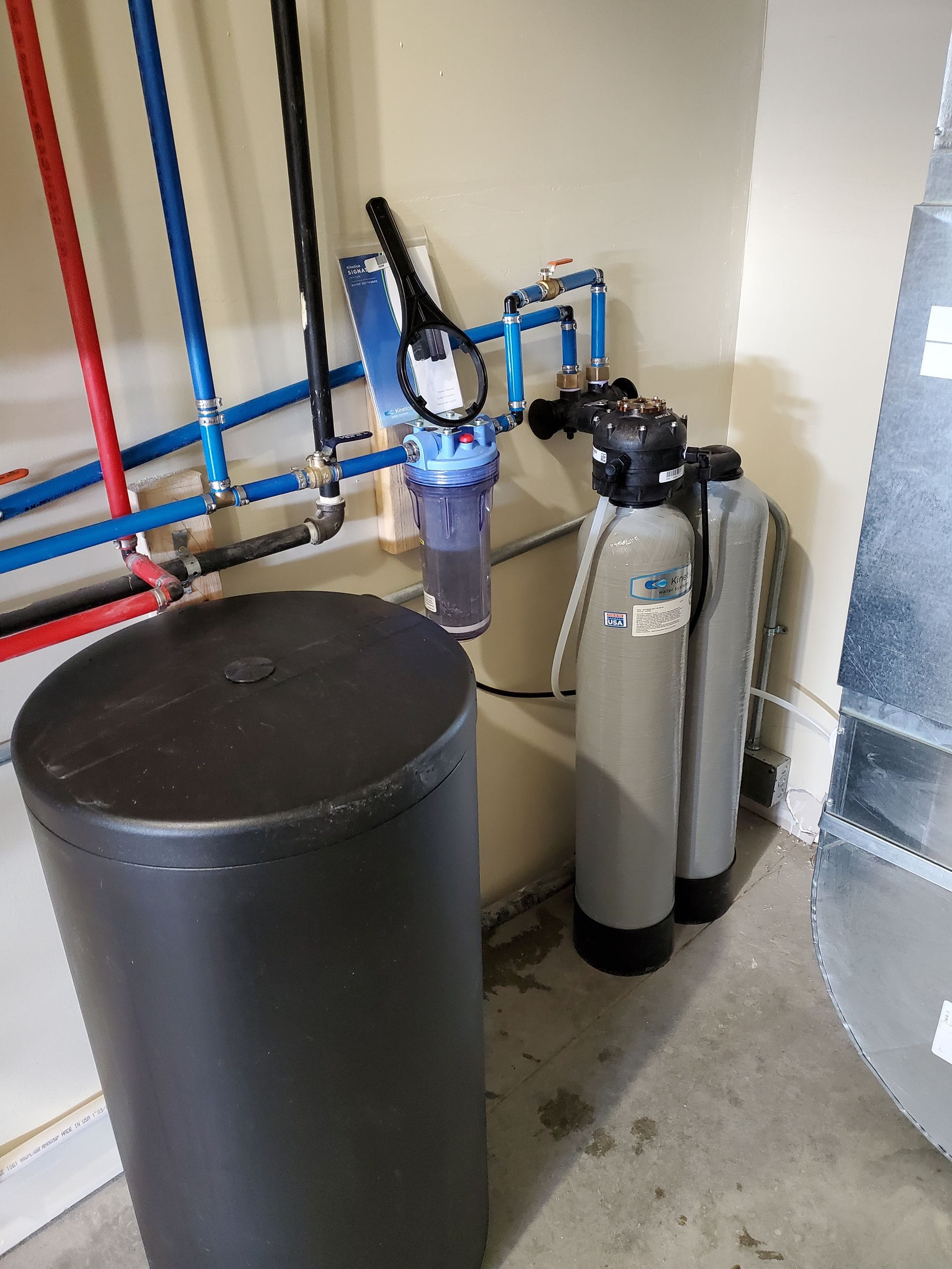 Water filtration system in a utility room with a black tank, two gray tanks, and blue and red pipes.