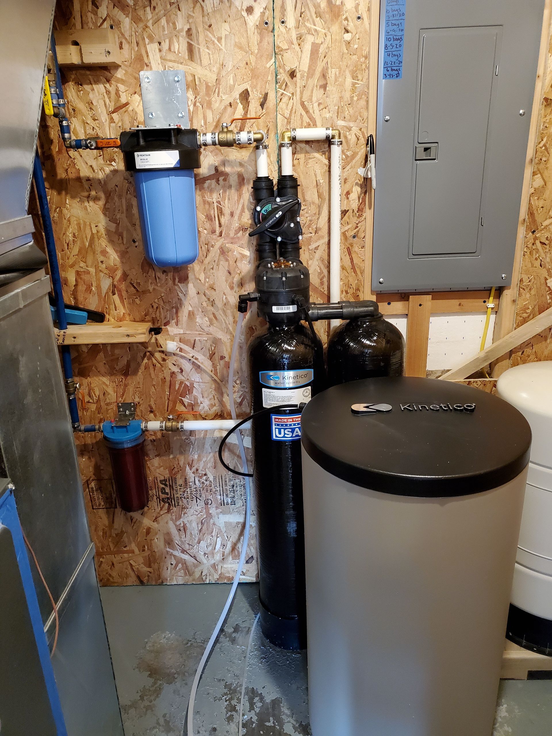 Water filtration and softening system in a basement setting; includes multiple tanks, filters, and piping.