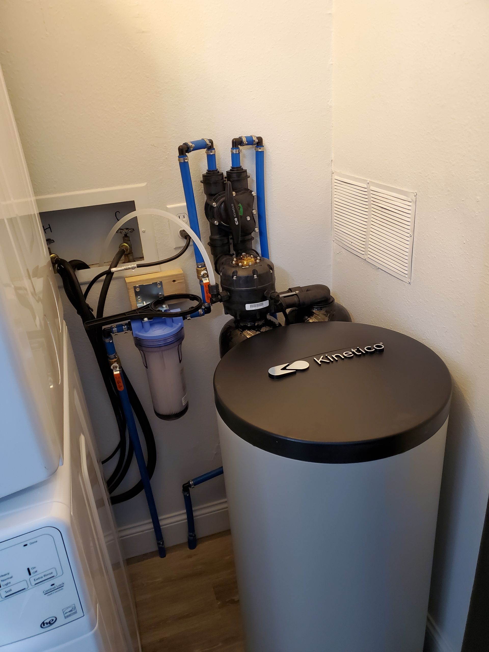 Water softener system in a utility closet with blue pipes and filter.