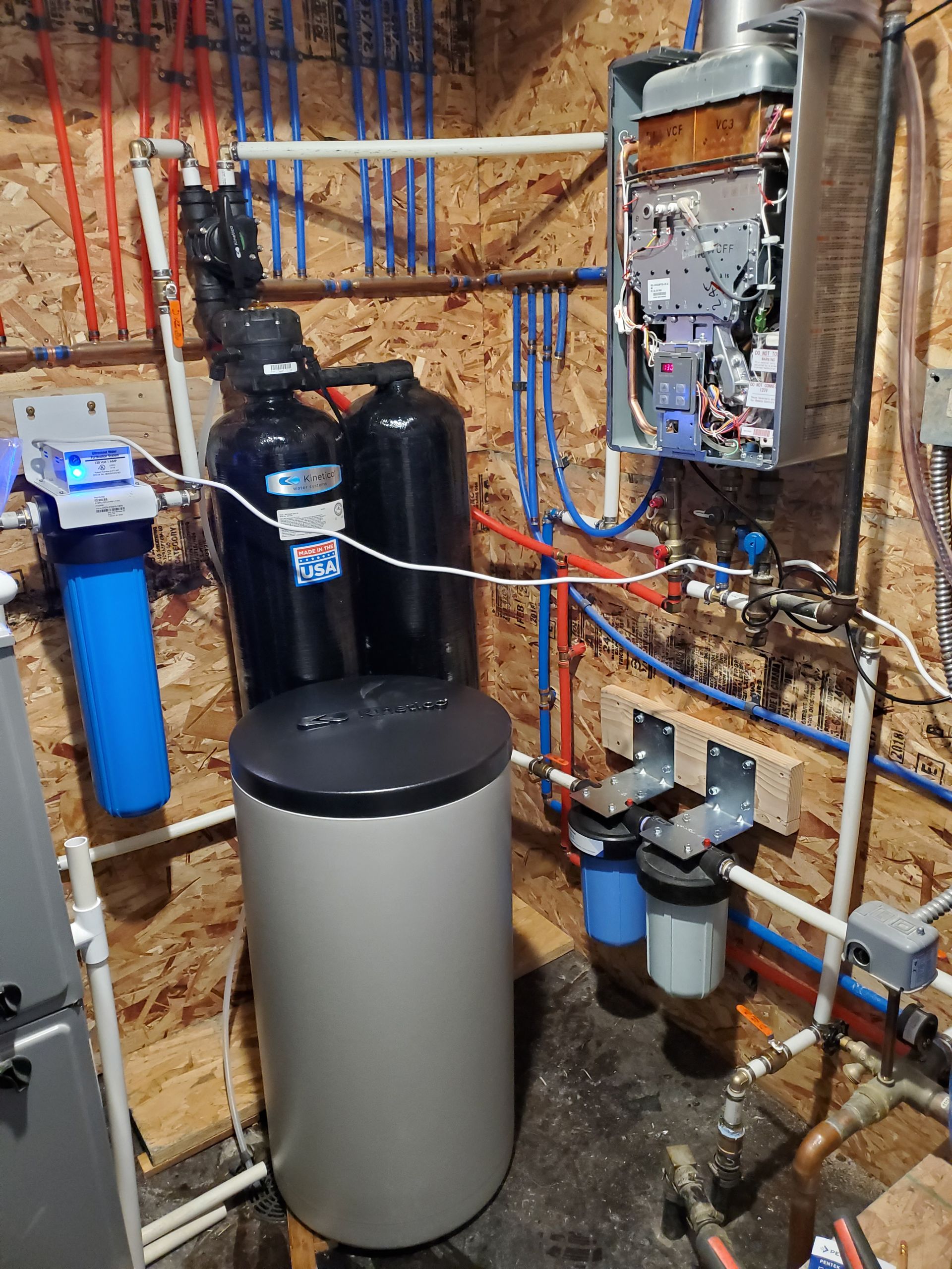 Plumbing system: water softener, filters, tank, and tankless water heater on a wood-paneled wall.