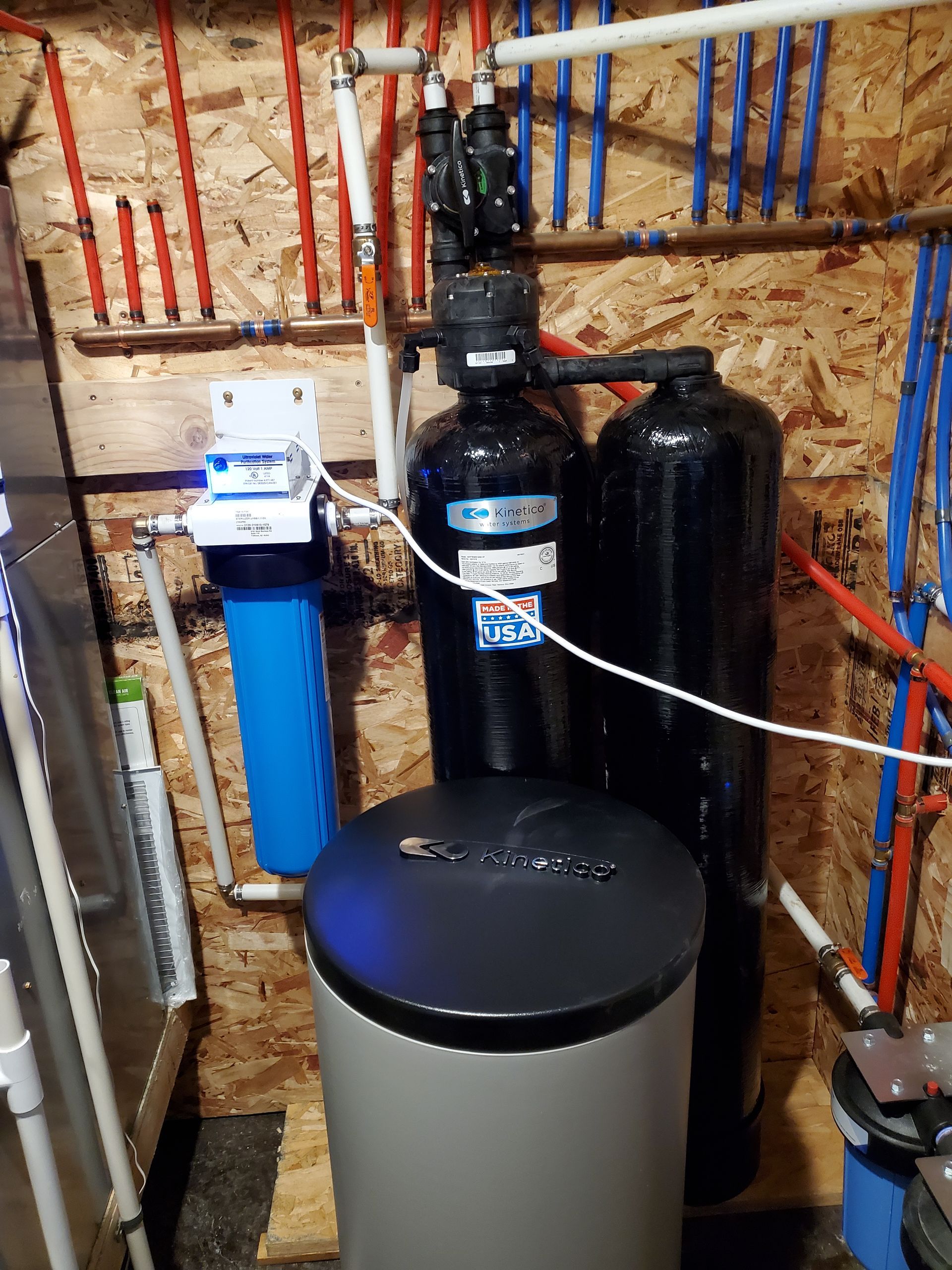 Water filtration and softening system in a basement.  Blue, black, and white tanks and pipes.