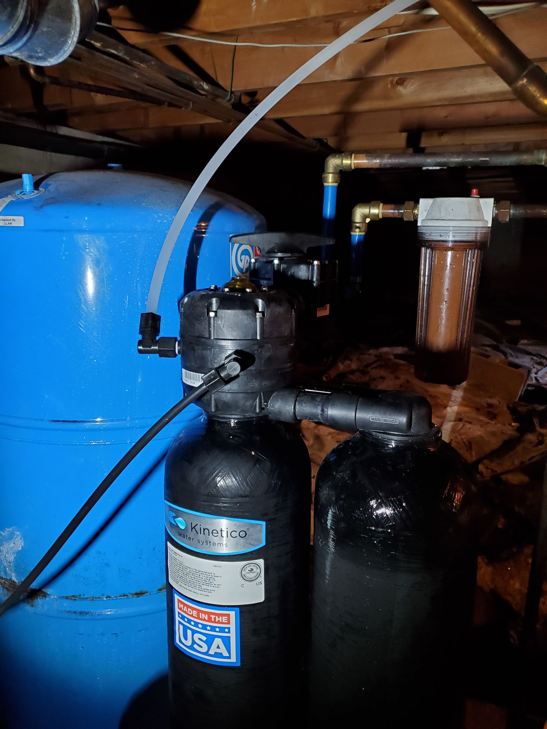 Water filtration system in a basement setting with blue tank, black tanks and a brown filter.