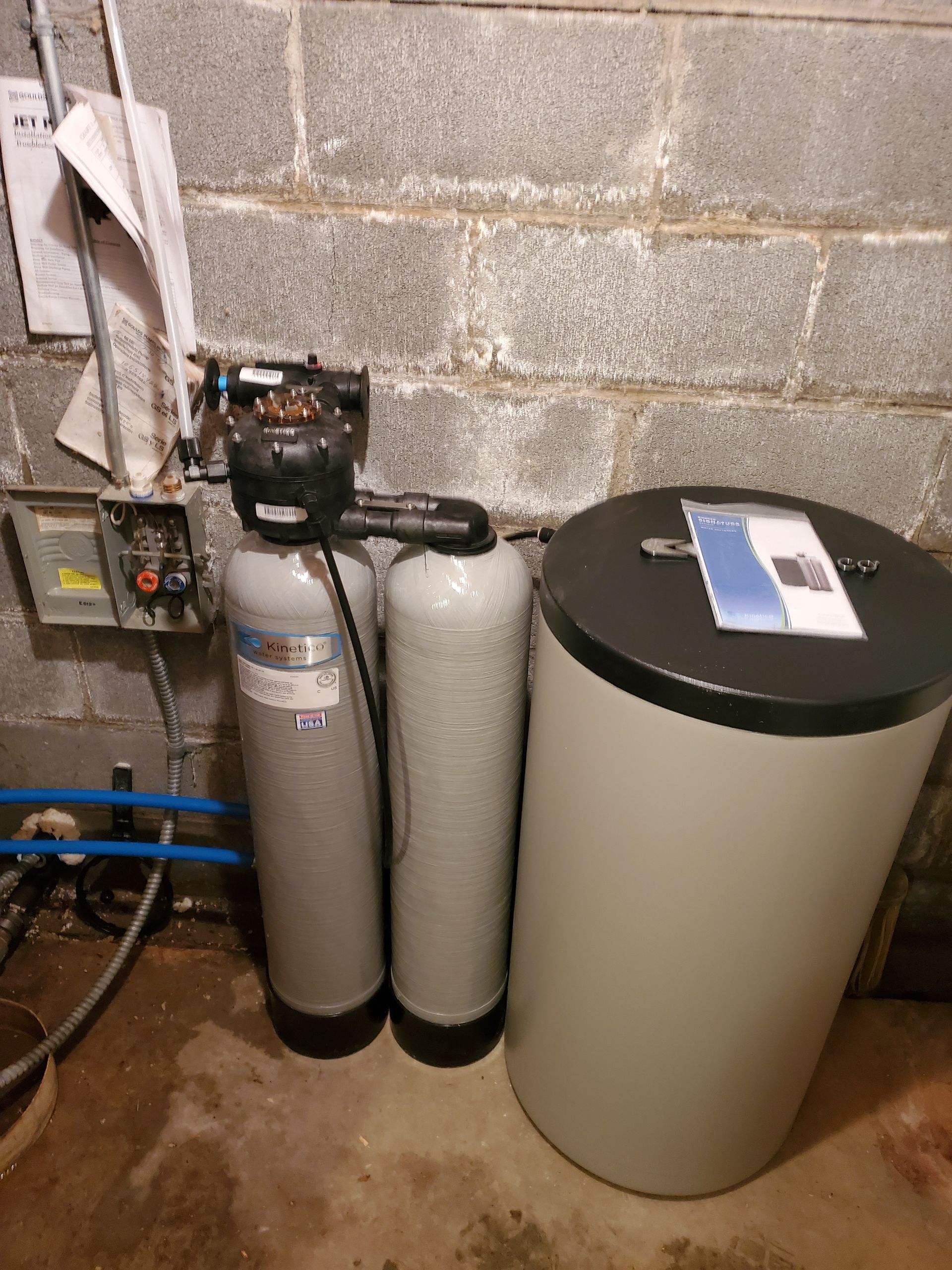 Water filtration system in a basement setting; gray tanks and black control unit.