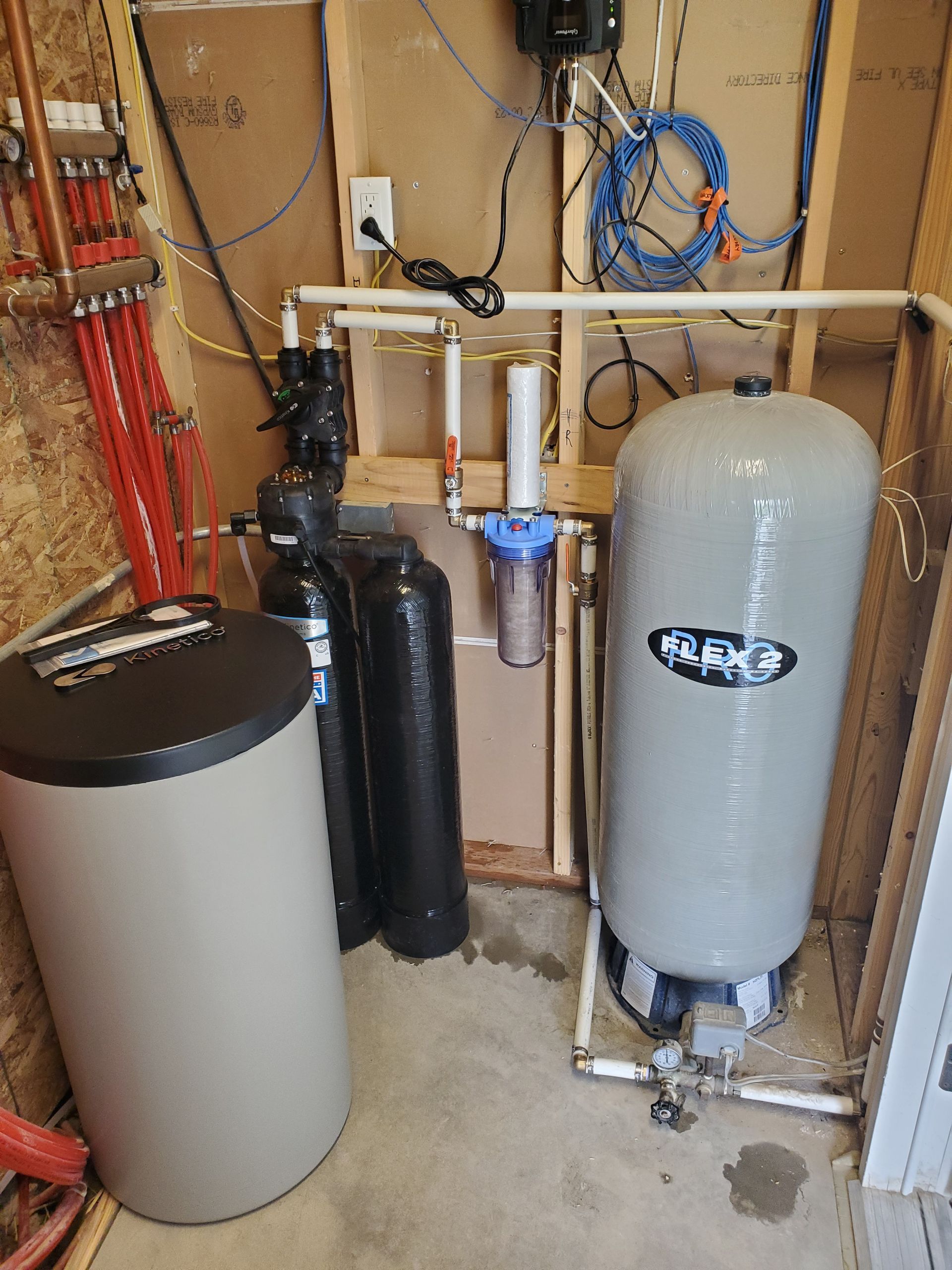 Water treatment system in a utility room with tanks, pipes, and electrical components.