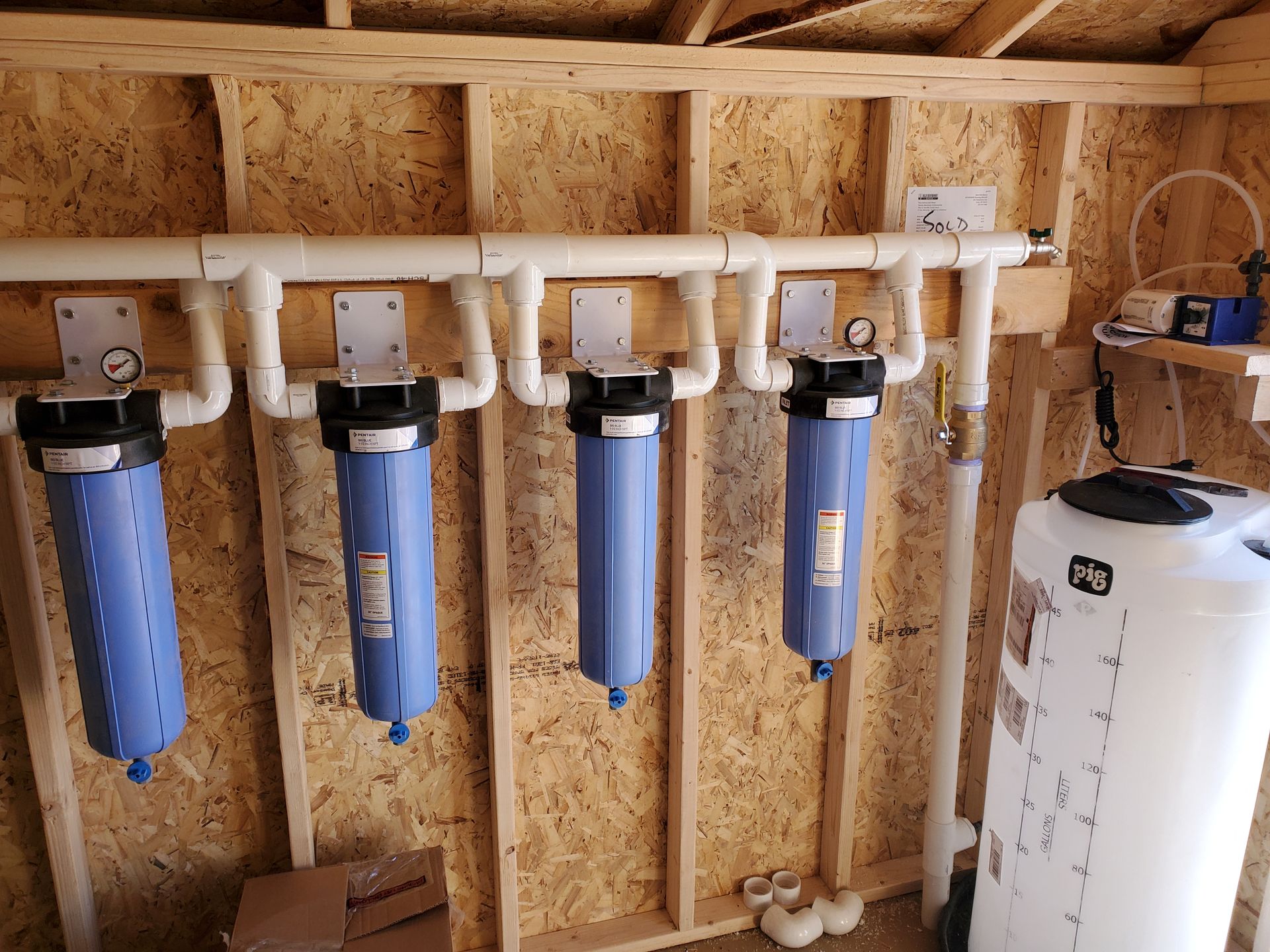 Water filtration system with four blue filter housings, white pipes, and a white tank.