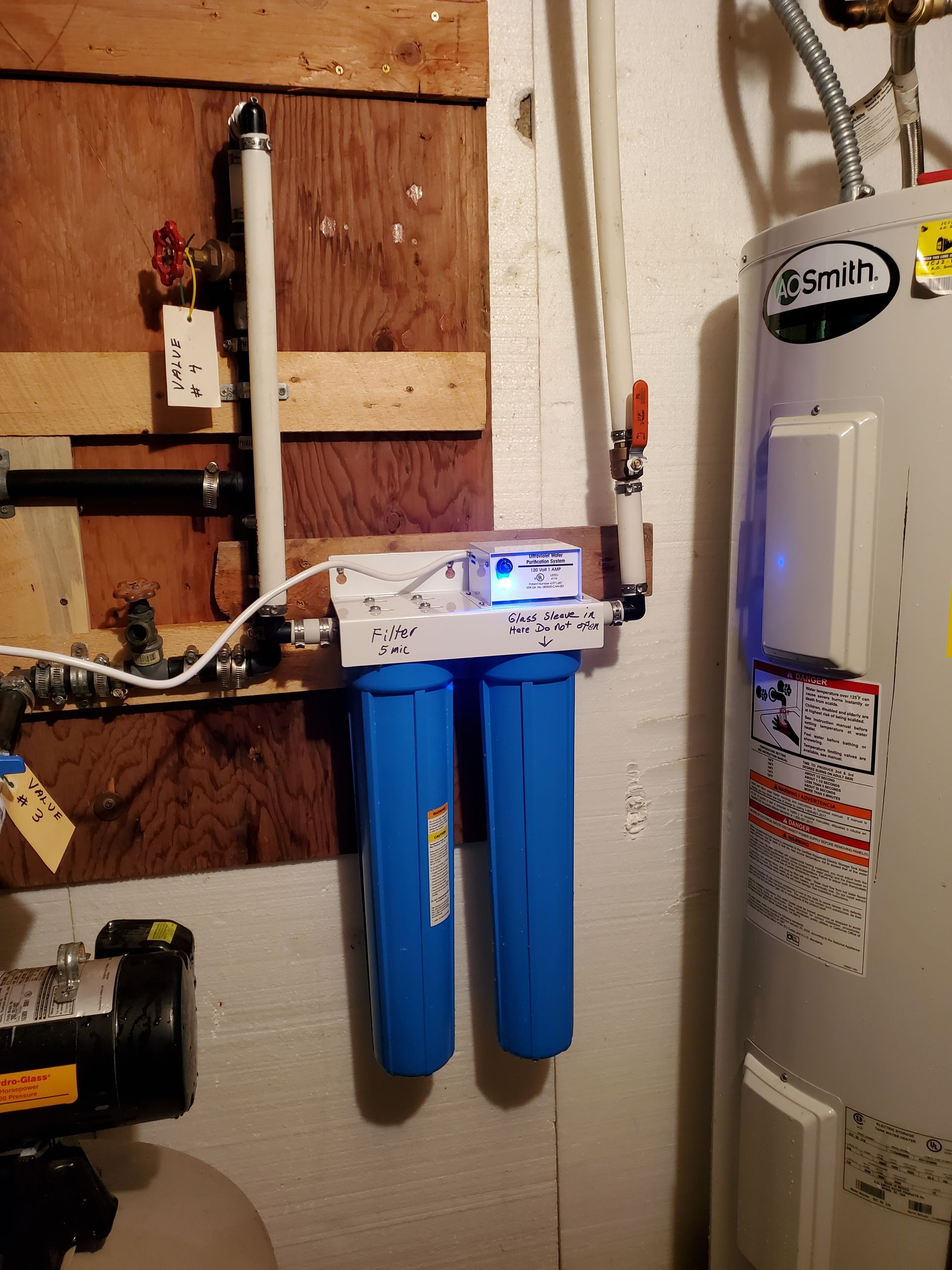 Blue water filter system installed near a water heater and pipes in a utility room.