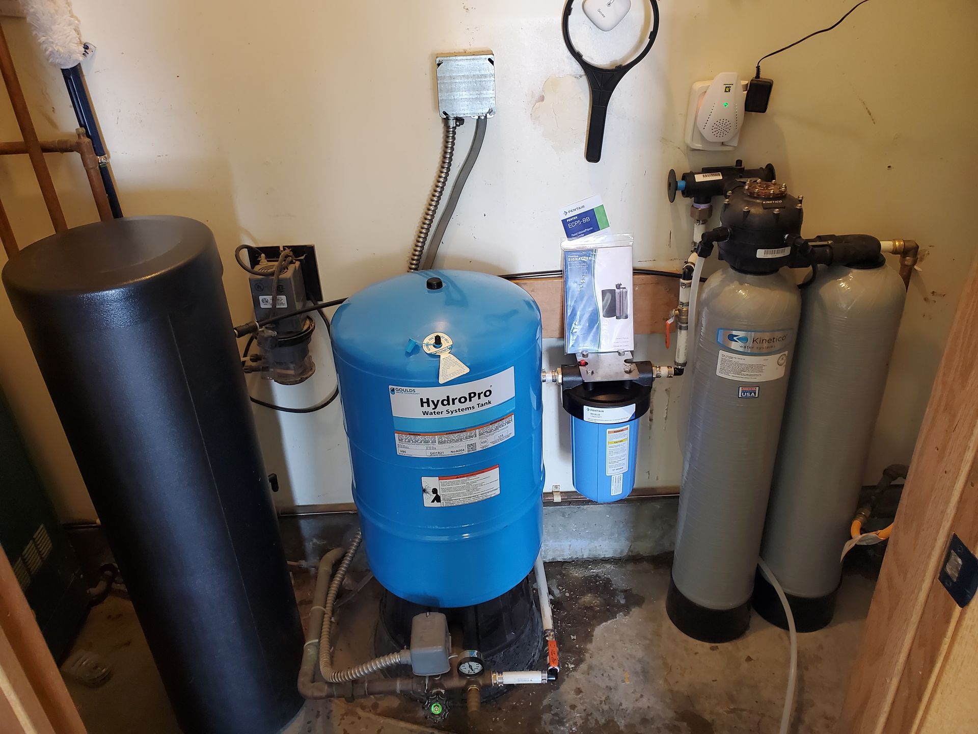 Water filtration and storage system in a utility room; a blue pressure tank, filters, and a black cylinder.