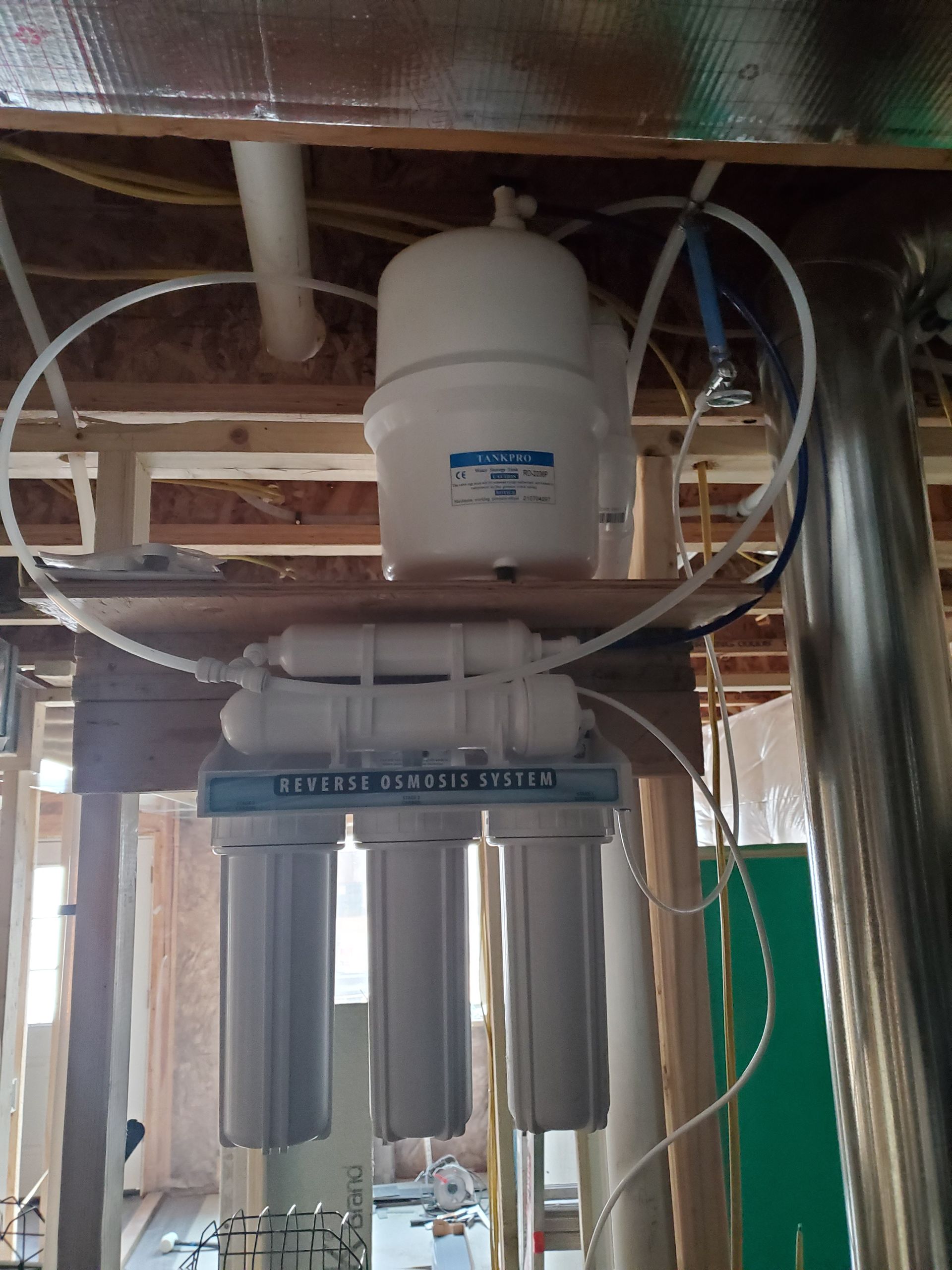 Reverse osmosis water filtration system installed in a basement, with various white filter canisters and a storage tank.