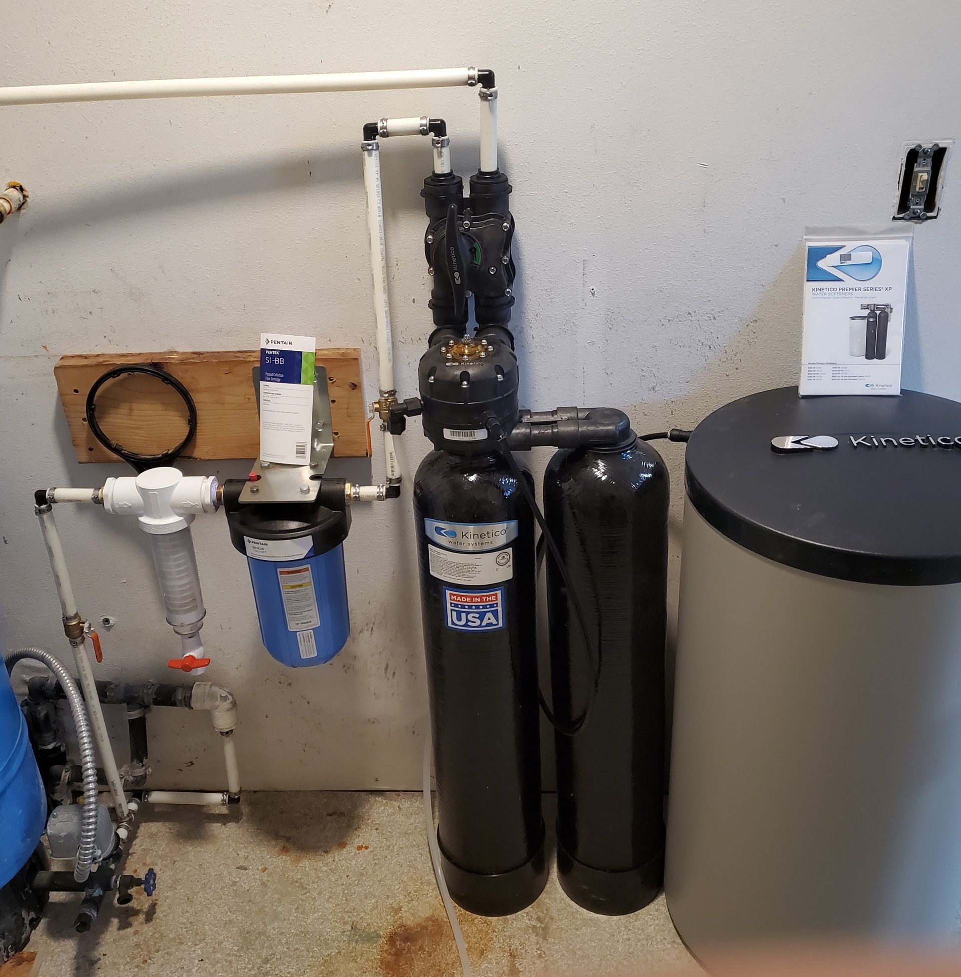 Water filtration system in a garage. Includes filter canisters, tank, pipes, and control valve.