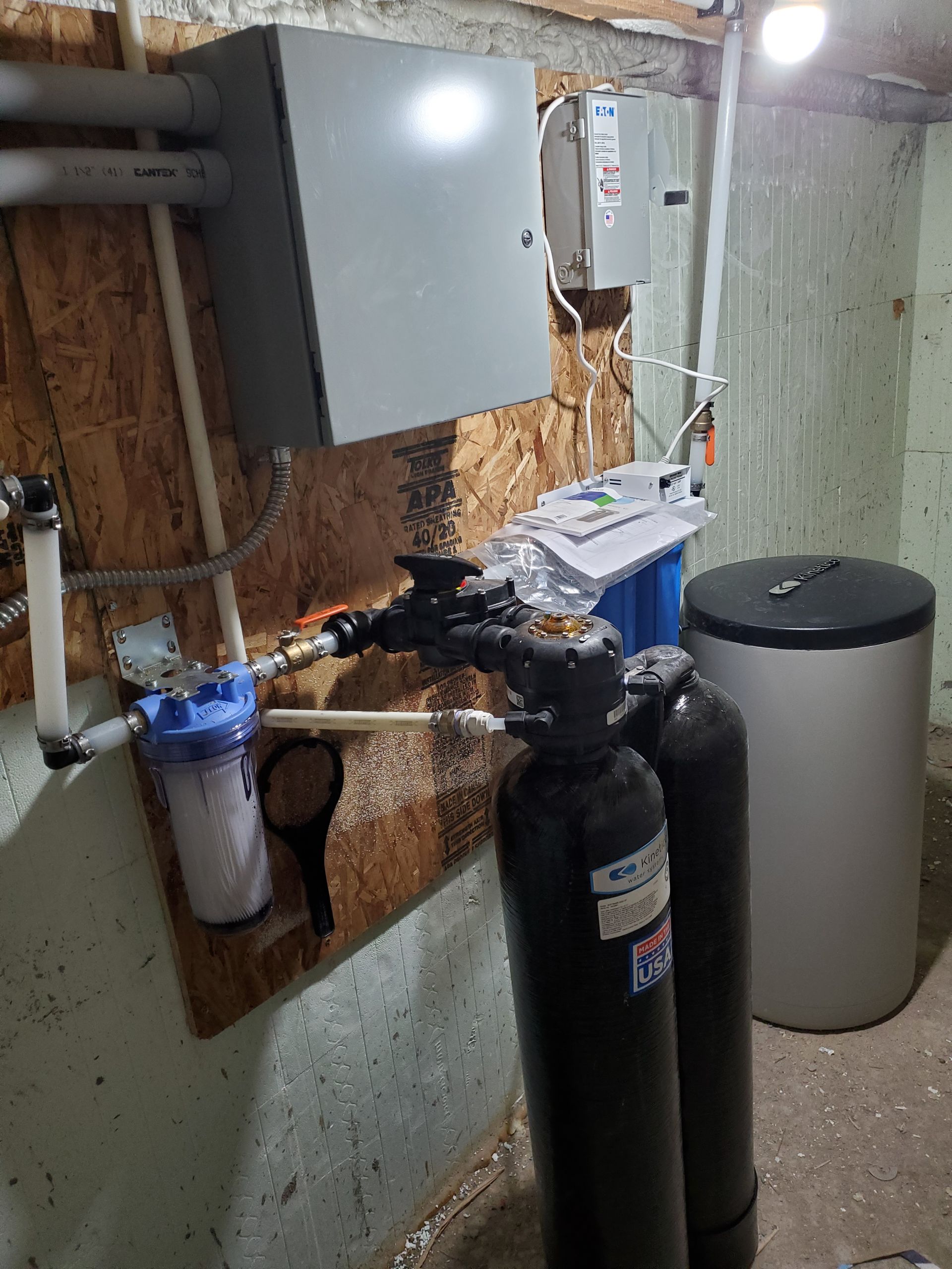 Water filtration system in a basement. Includes tanks, filters, and a water heater.