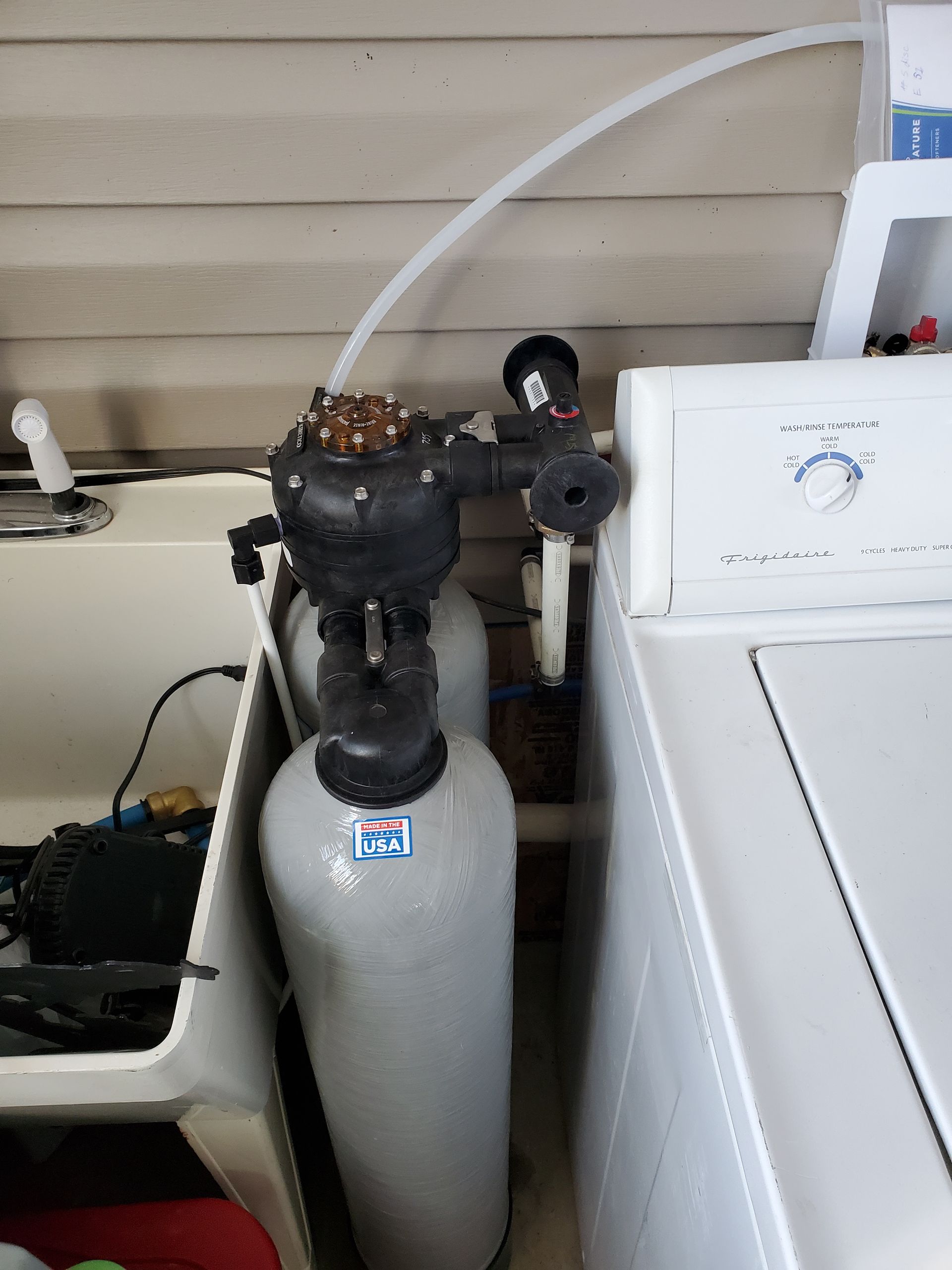 Water softener and filter system next to a washing machine in a utility room.