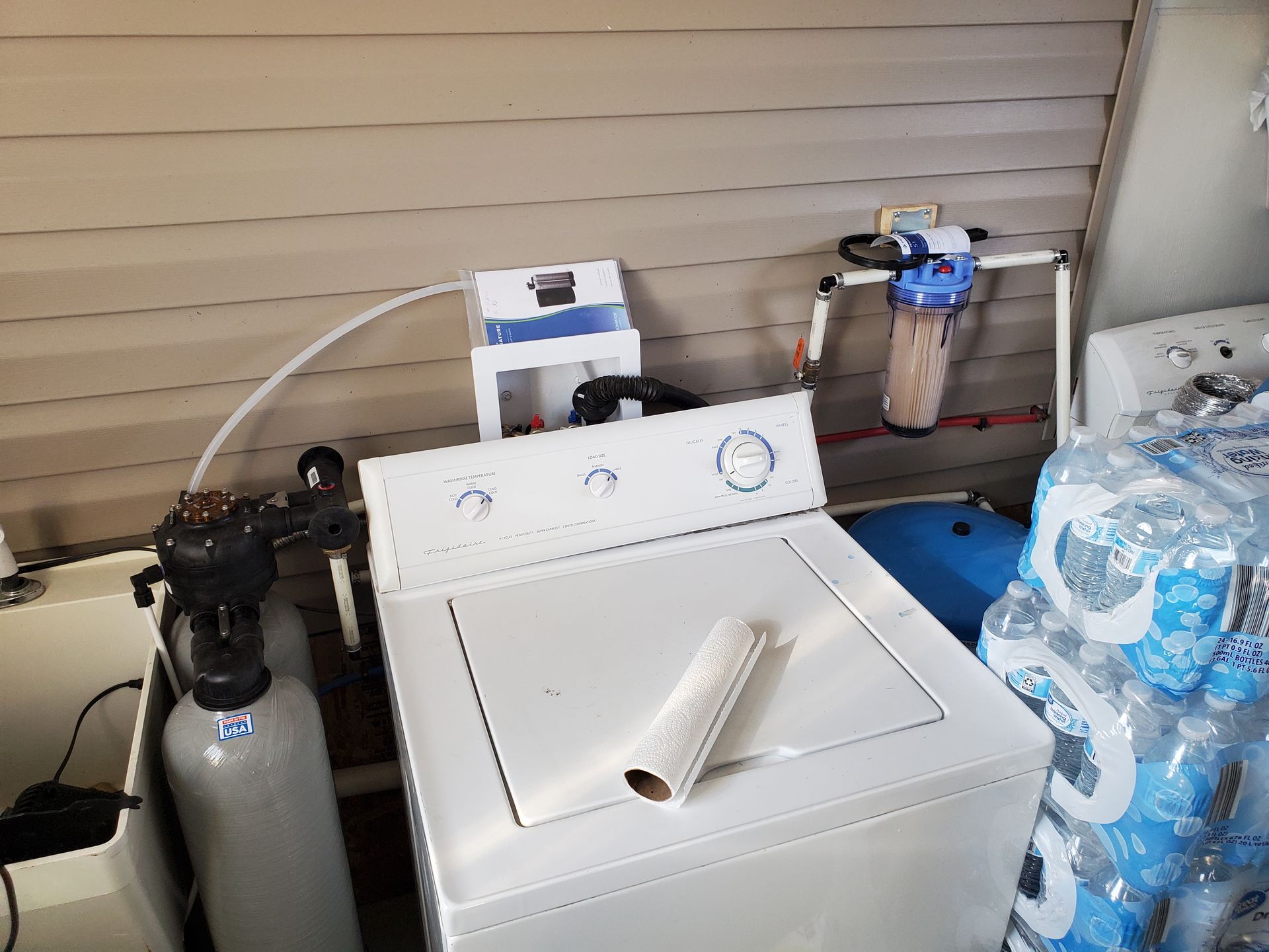 Washing machine with water filtration system, water bottles in utility room setting.